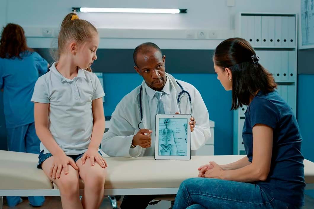 Doctor showing X-ray on tablet to child and parent in a clinic examination room.