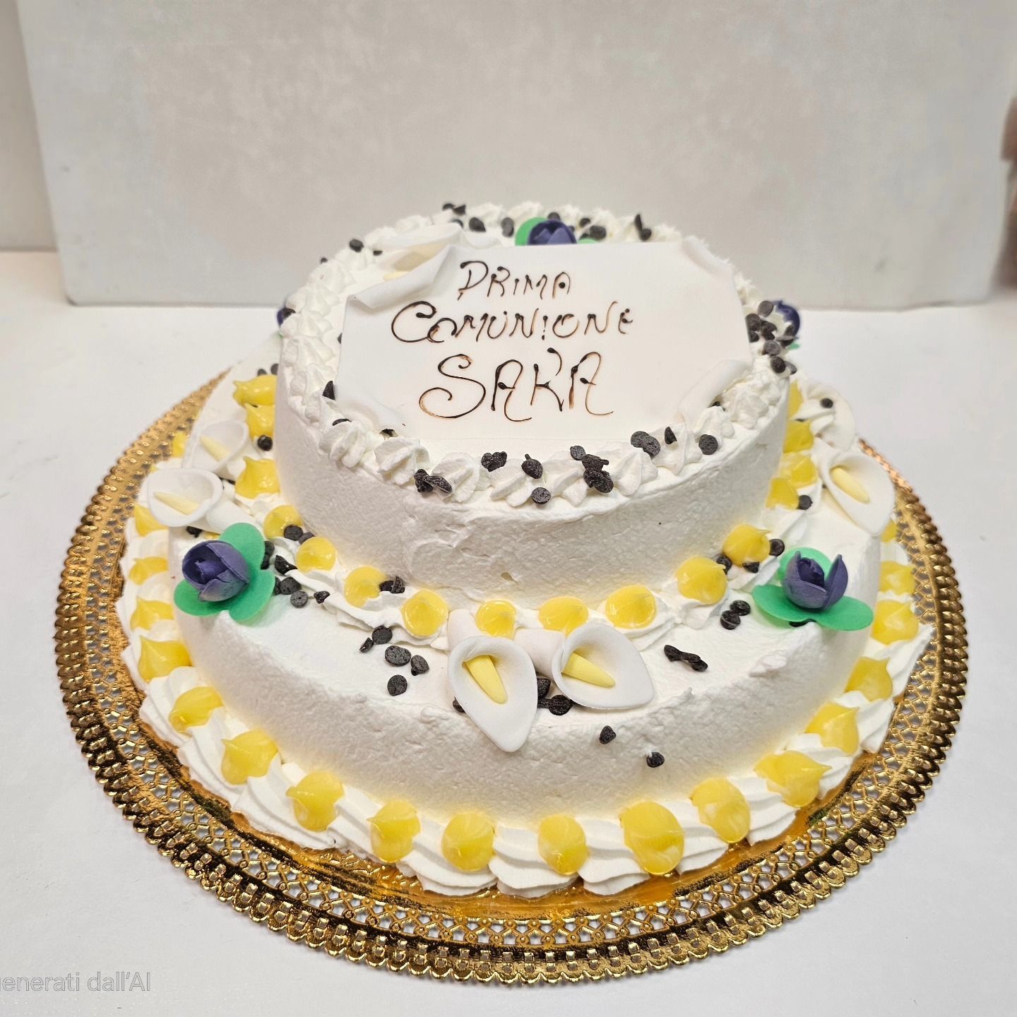 Torta a due piani bianca con decorazioni gialle e fiori, sormontata dalla scritta