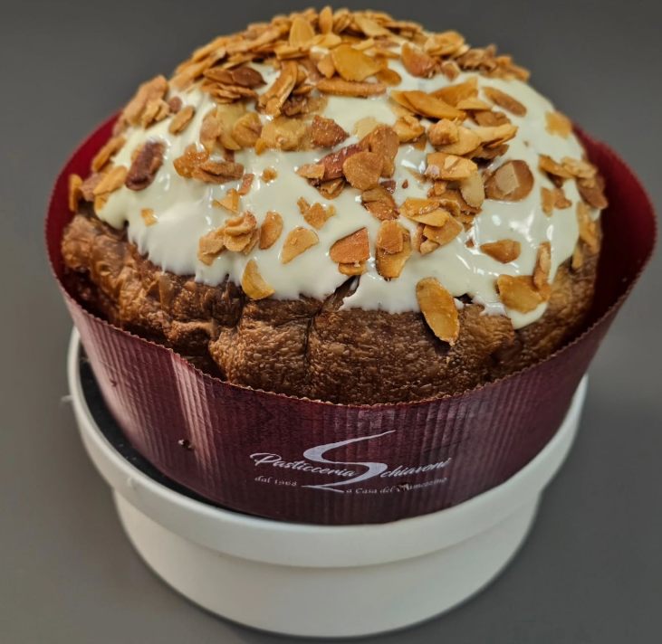 Muffin ricoperto di glassa bianca e noci tritate, servito in un pirottino di carta marrone su un piatto bianco.