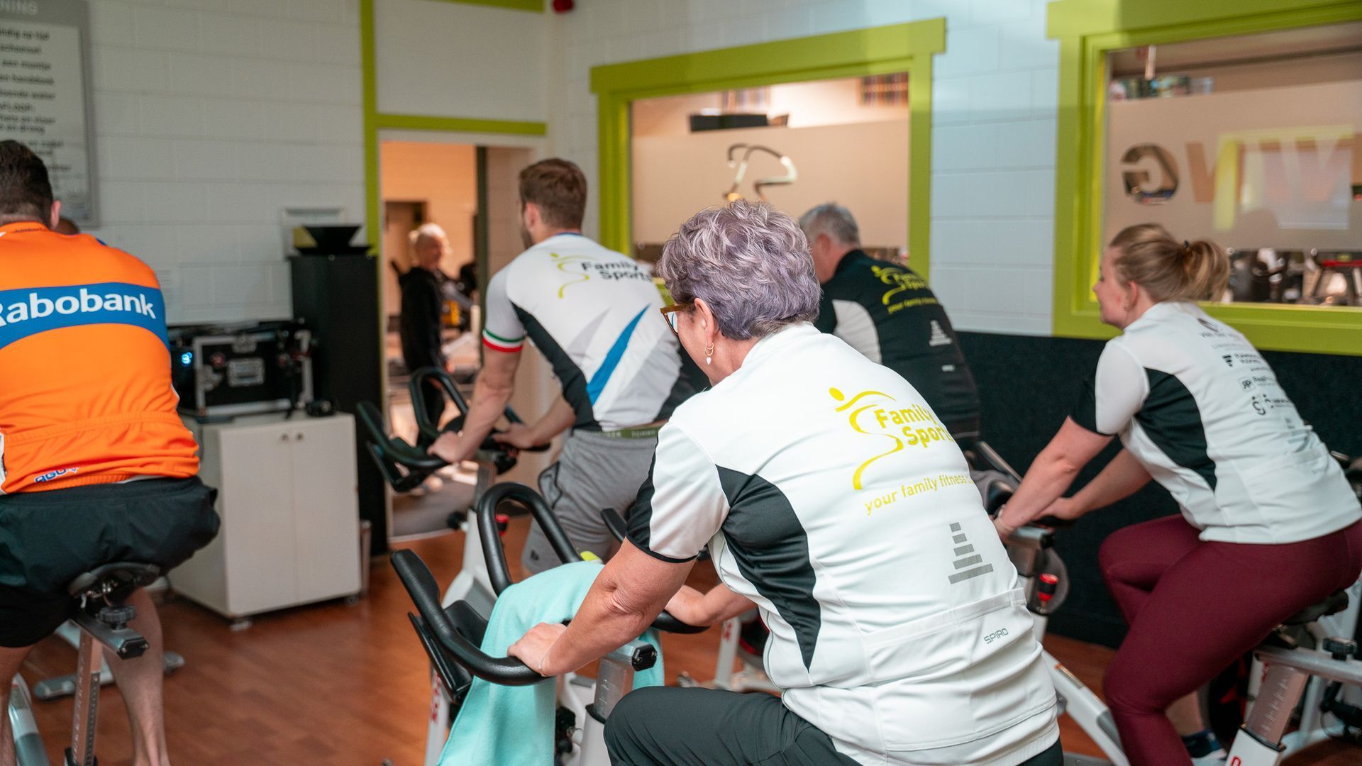 Mensen die sporten op hometrainers in een lichte, overdekte fitnessruimte.