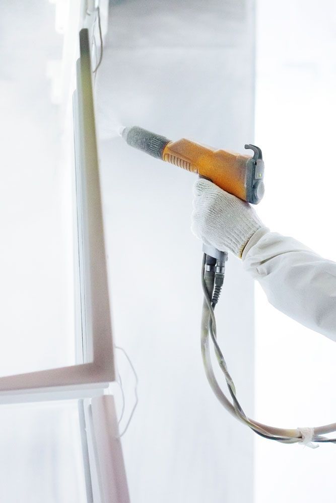 Person powder coating a white frame with an orange spray gun.