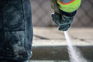 A person is using a high pressure washer to clean a concrete surface.