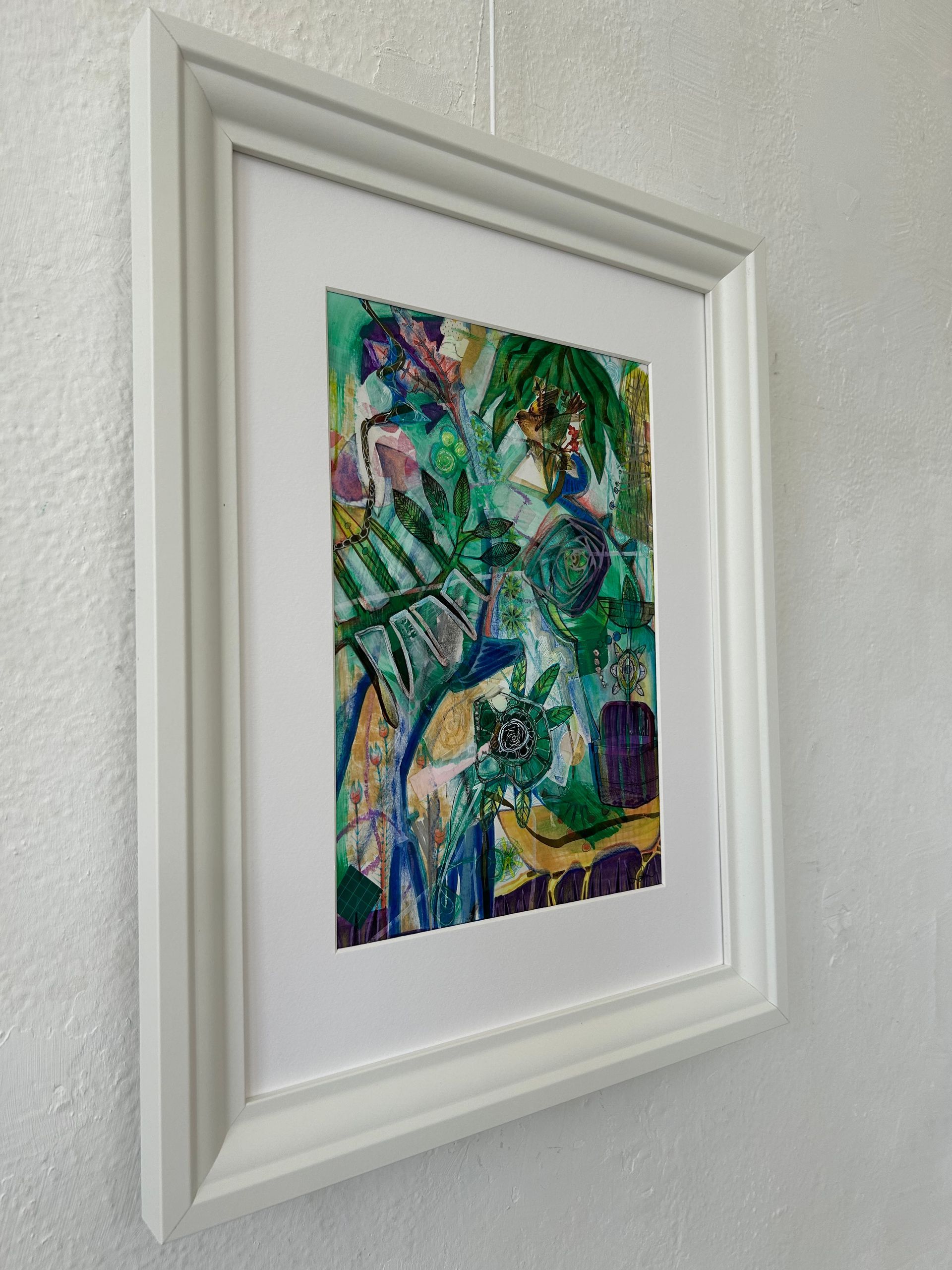 Ingelijst abstract schilderij met groene, blauwe en paarse penseelstreken op een witte muur.