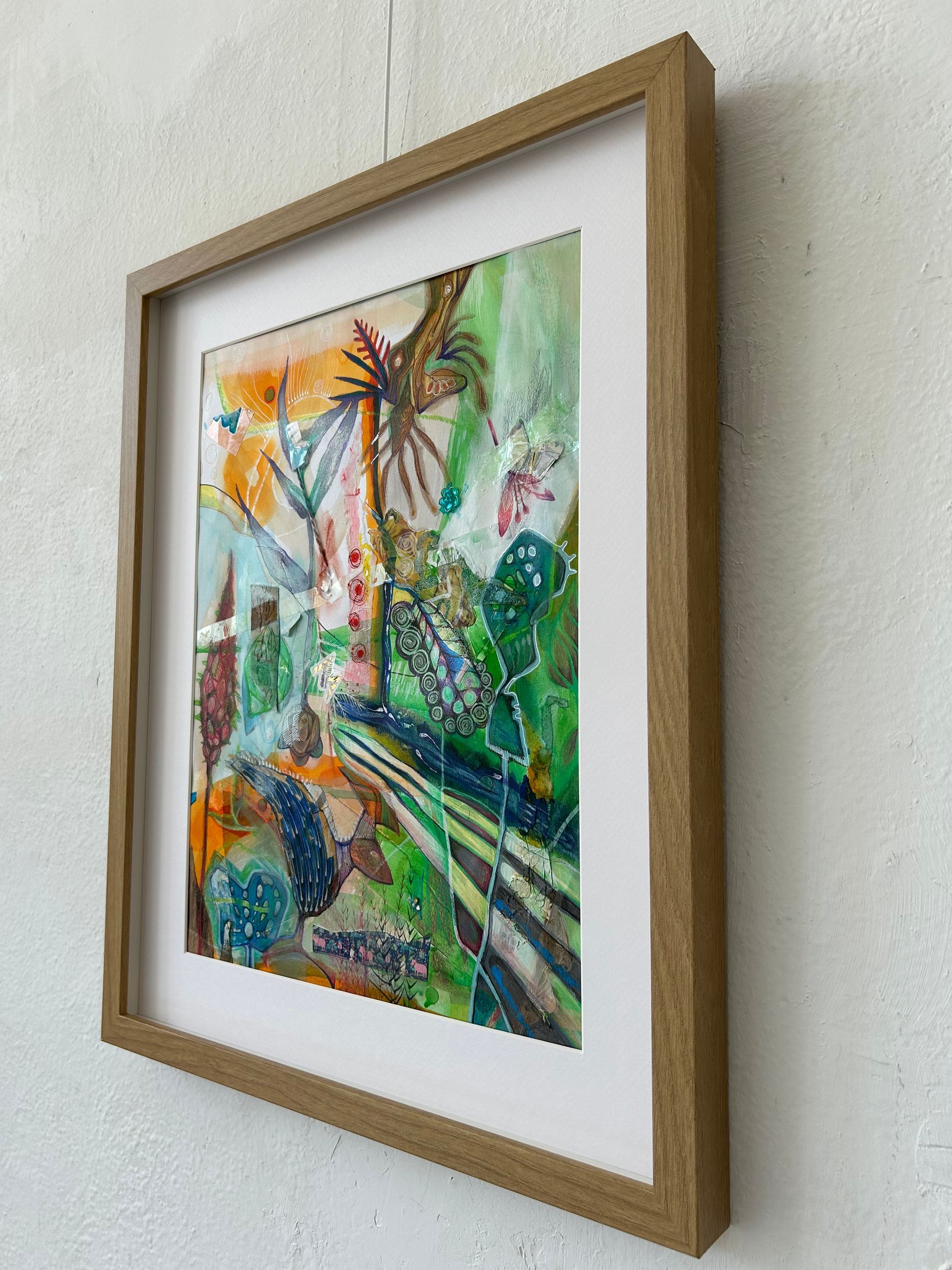 Ingelijst abstract aquarel met groene, blauwe, oranje en gele accenten aan de muur.