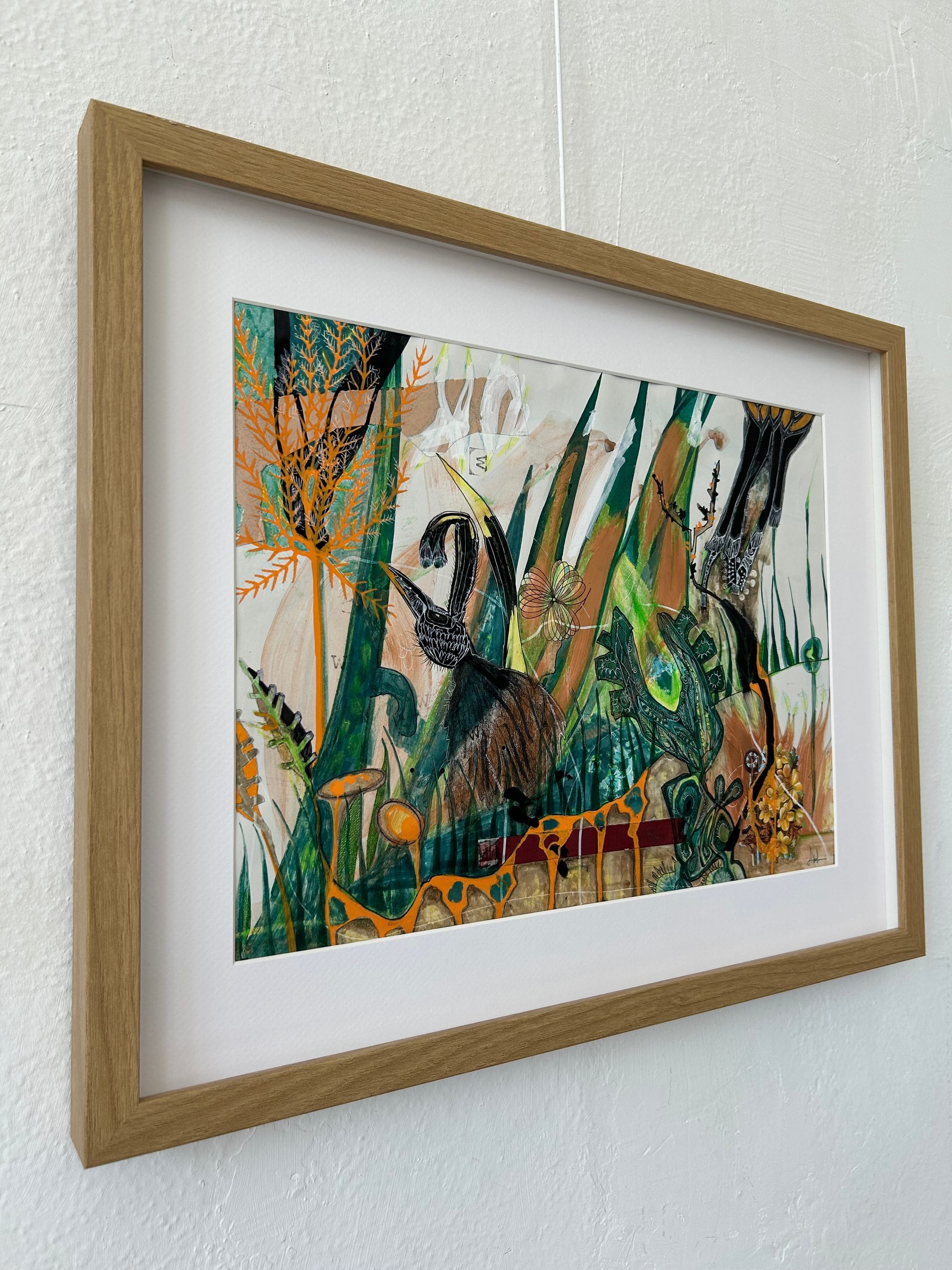 Ingelijst abstract schilderij met groene, oranje en zwarte penseelstreken op een witte muur.