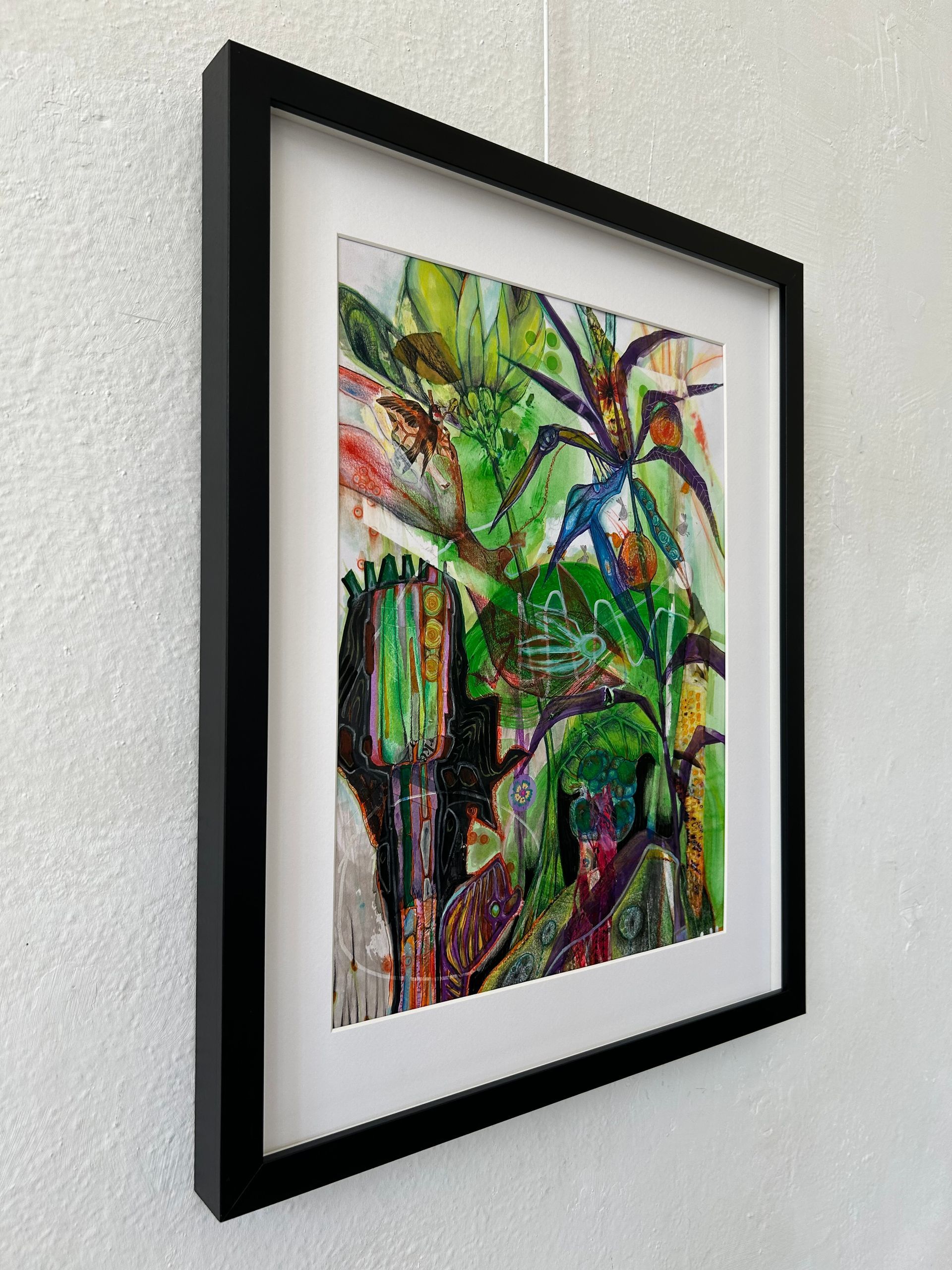 Ingelijst abstract schilderij met felgroene, rode en blauwe penseelstreken op een witte muur.