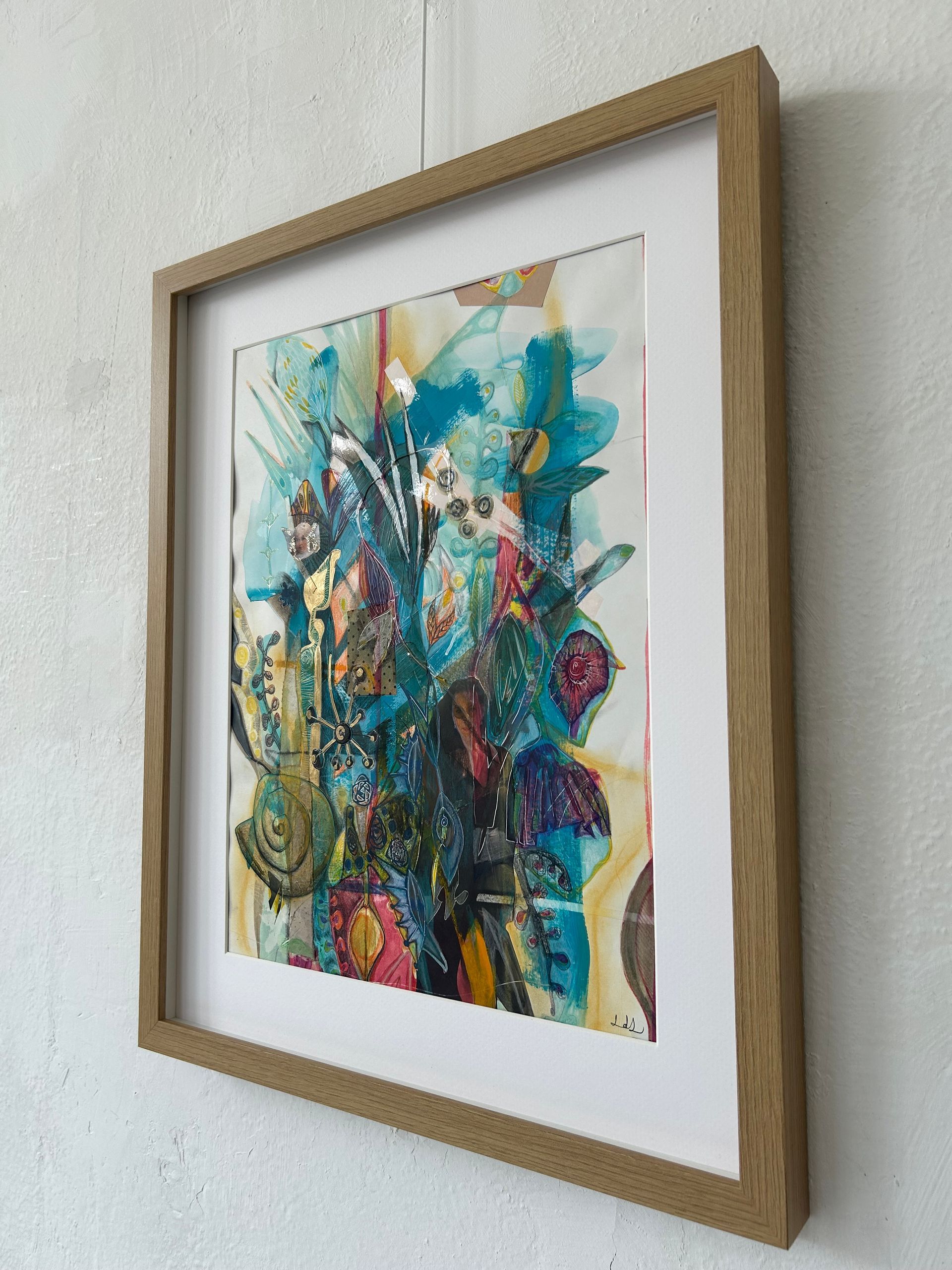 Ingelijst, kleurrijk abstract schilderij met turquoise, roze en goudtinten op een witte muur.