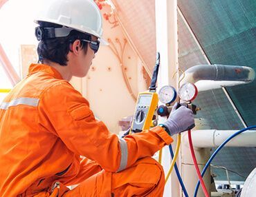 A man in an orange jumpsuit is working on a machine.