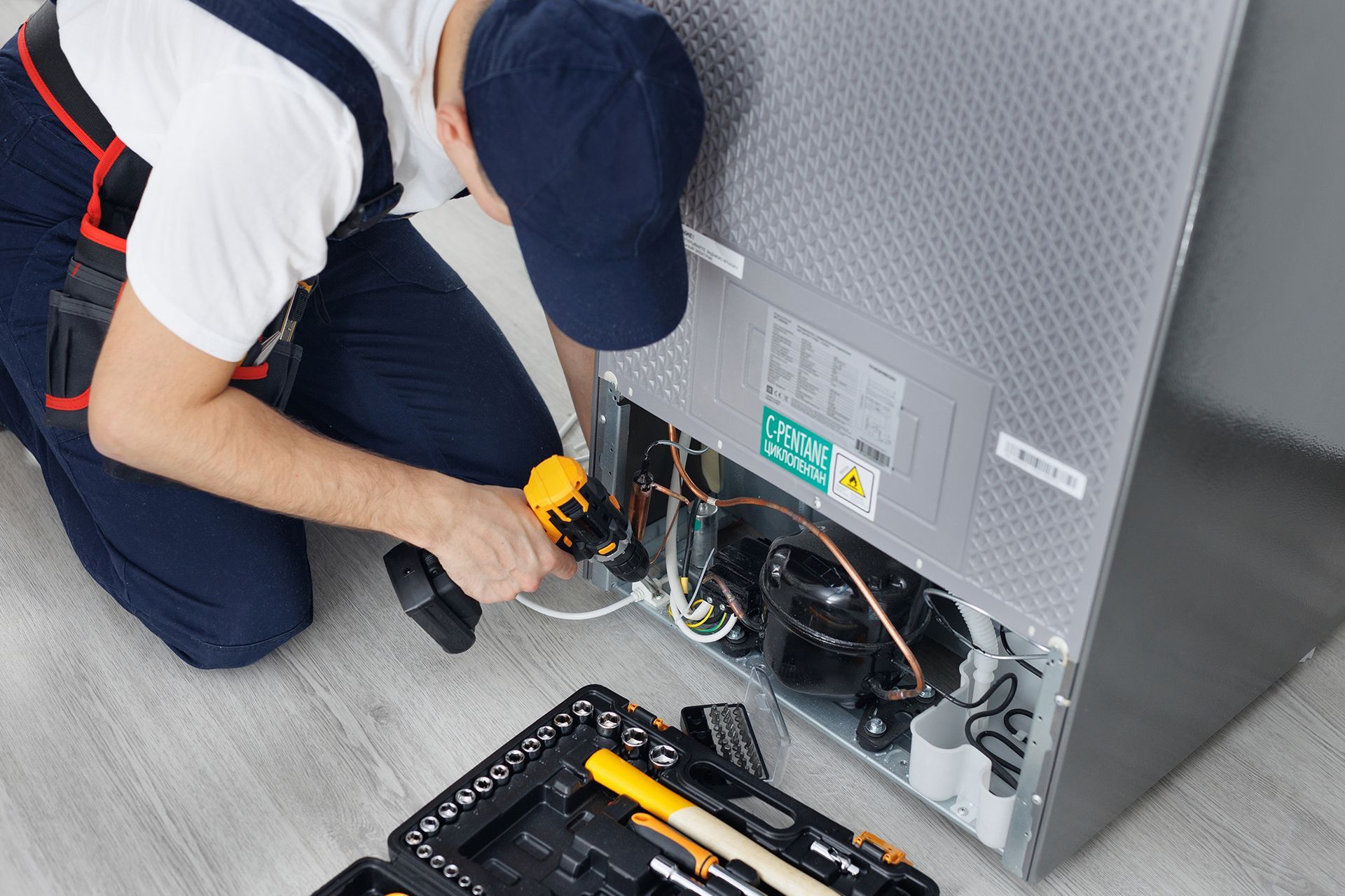 A man is fixing a refrigerator with a drill.
