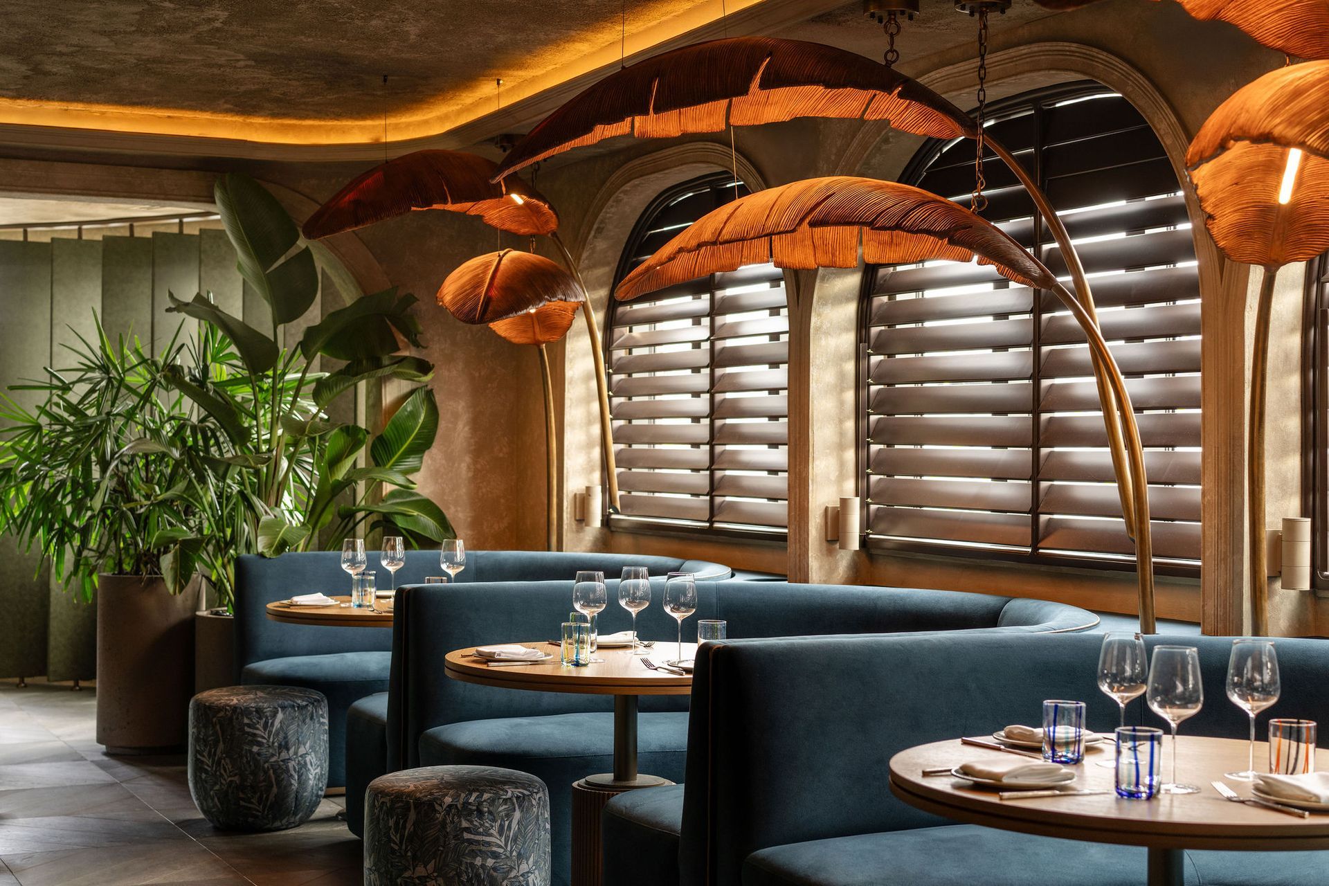 Interior of the dining room at the Harbour Club in Miami Beach showing two tables with cushioned teal chairs and two chandeliers.
