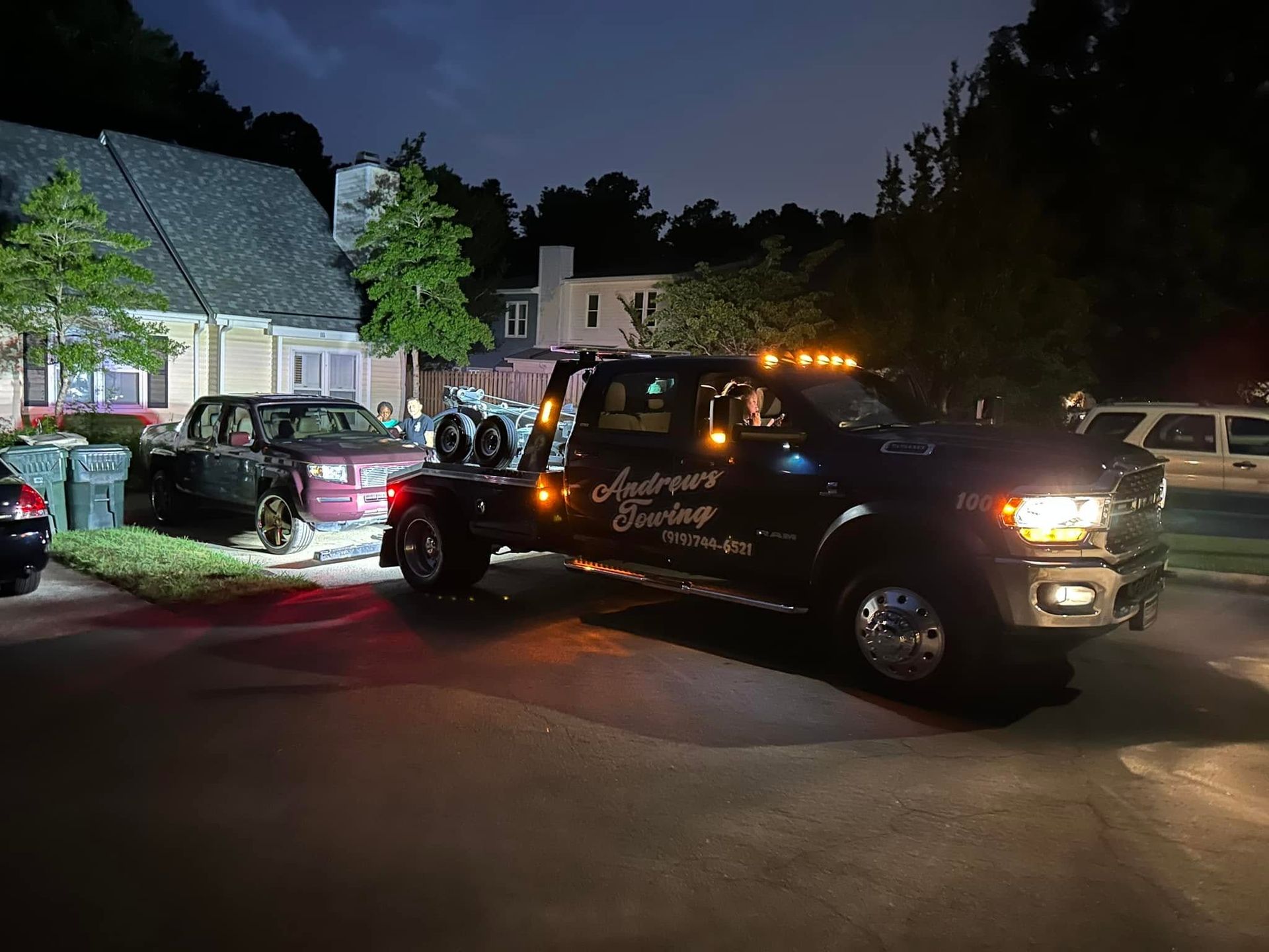 A tow truck is towing a car in a parking lot at night.