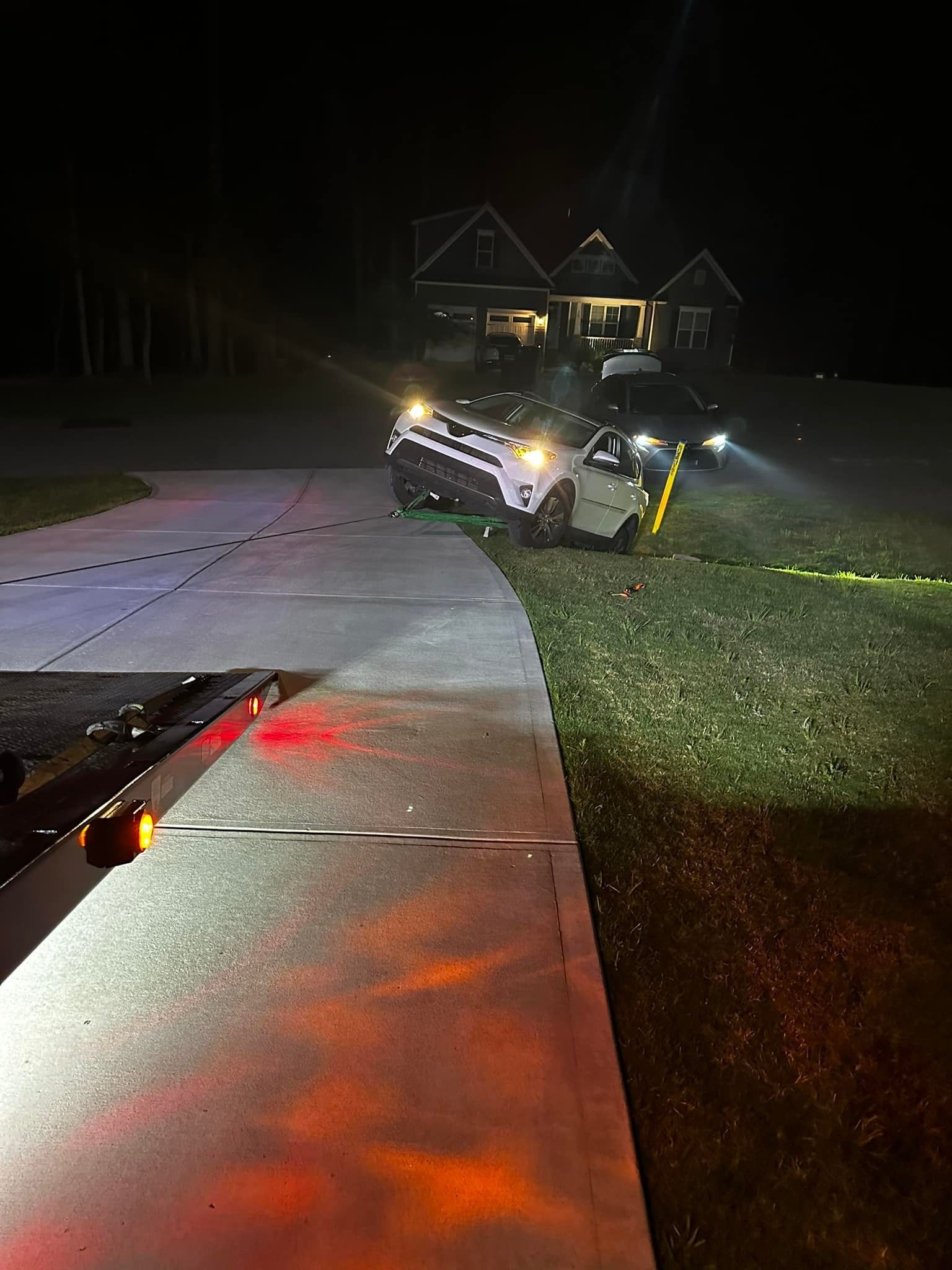 A car is being towed away from a house at night.