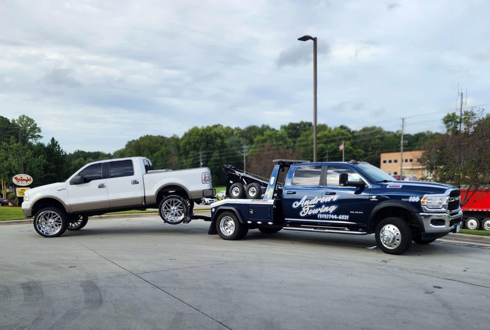 A white truck is being towed by a blue tow truck.