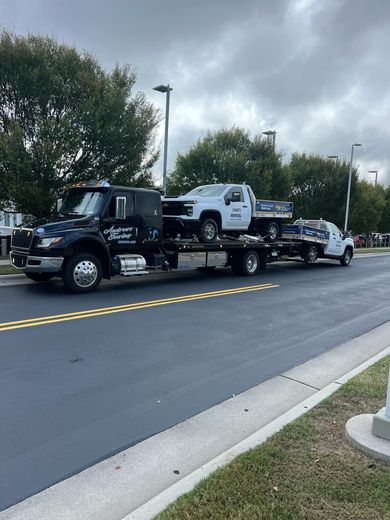A tow truck is carrying two cars down a street.
