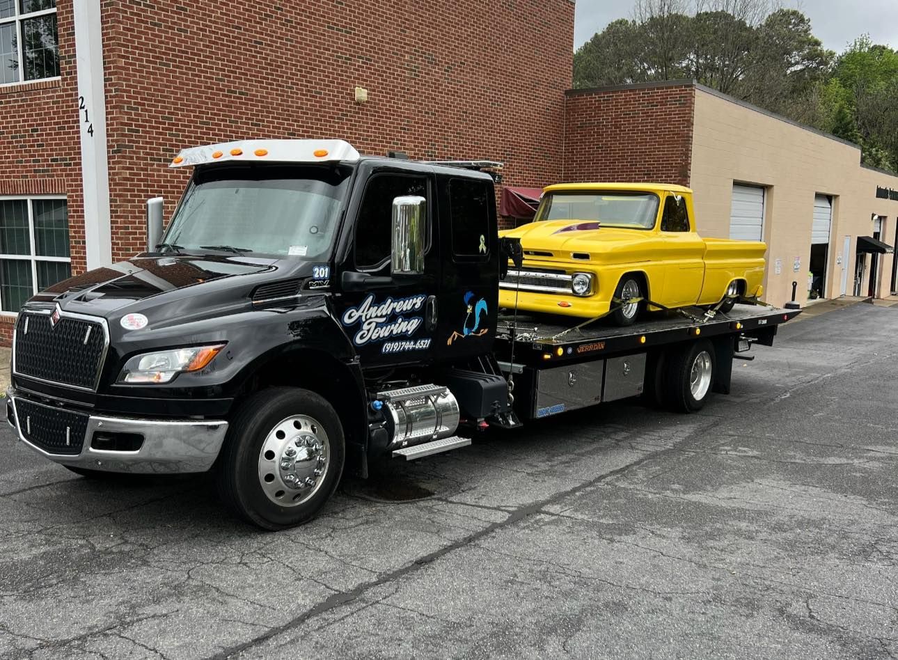 A black tow truck with a yellow truck on the back is parked in front of a brick building.