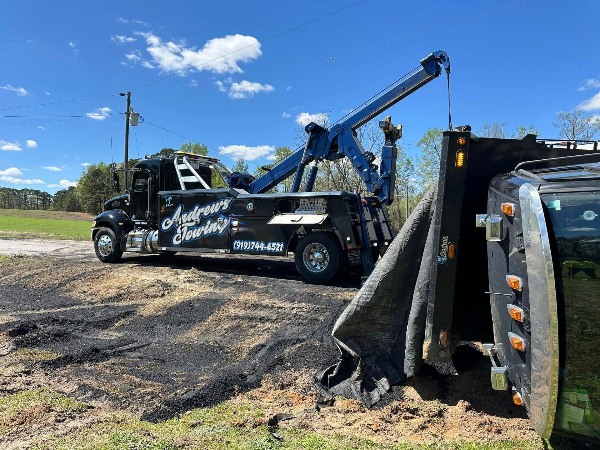 A tow truck is sitting on the side of the road next to a tractor.