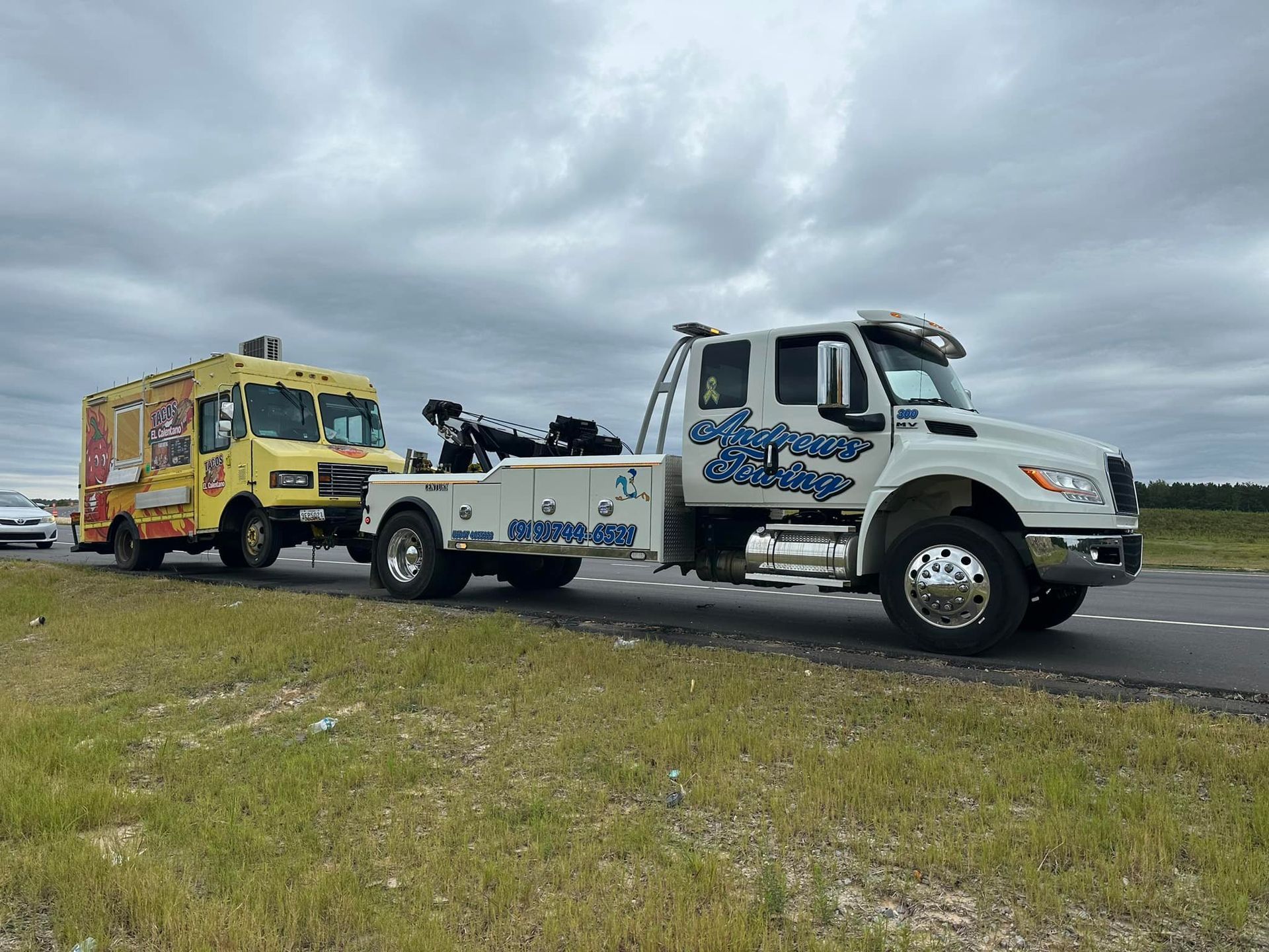 A tow truck is towing a yellow food truck on the side of the road.
