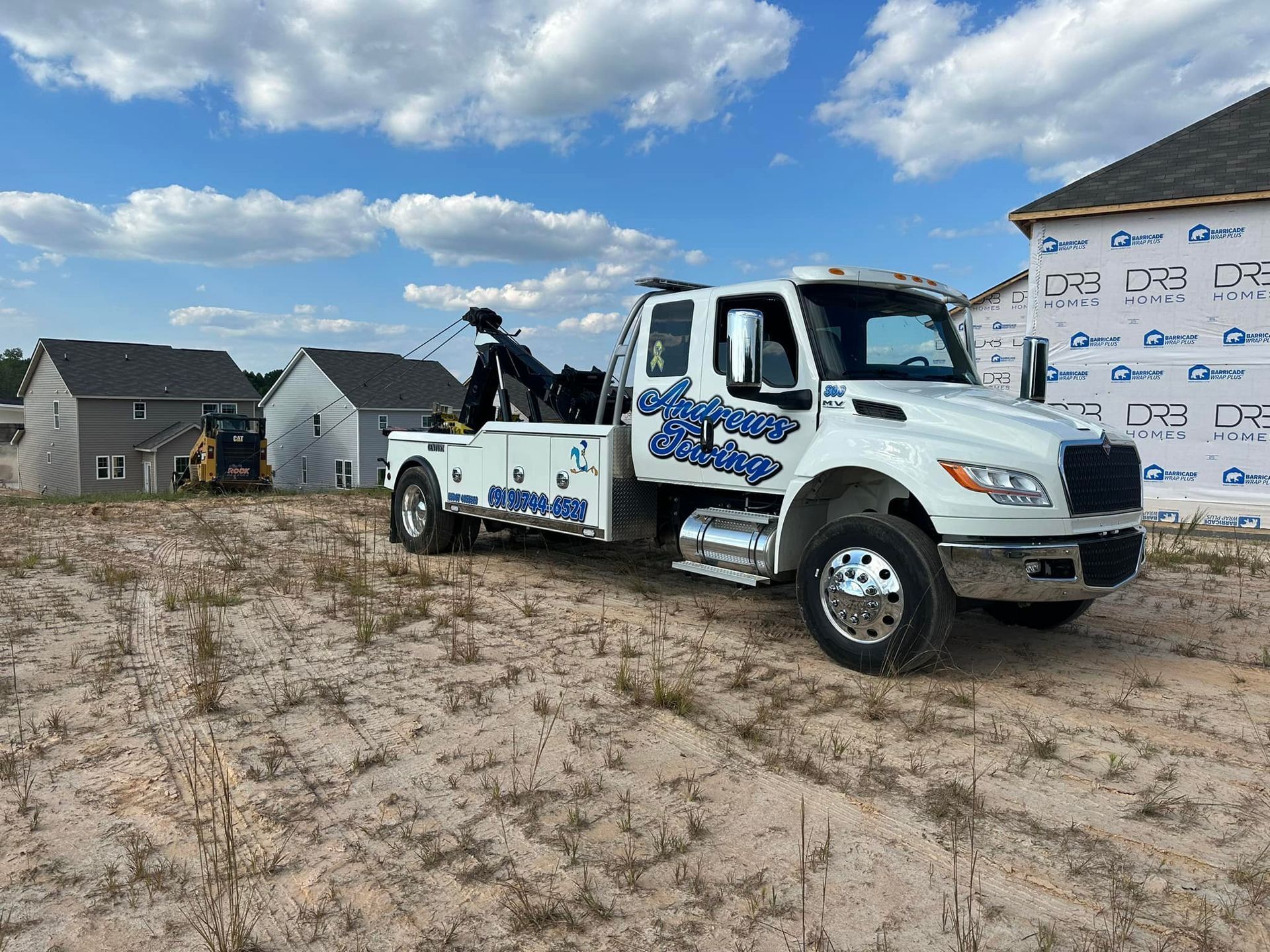 A white tow truck is parked in a dirt field in front of a house.