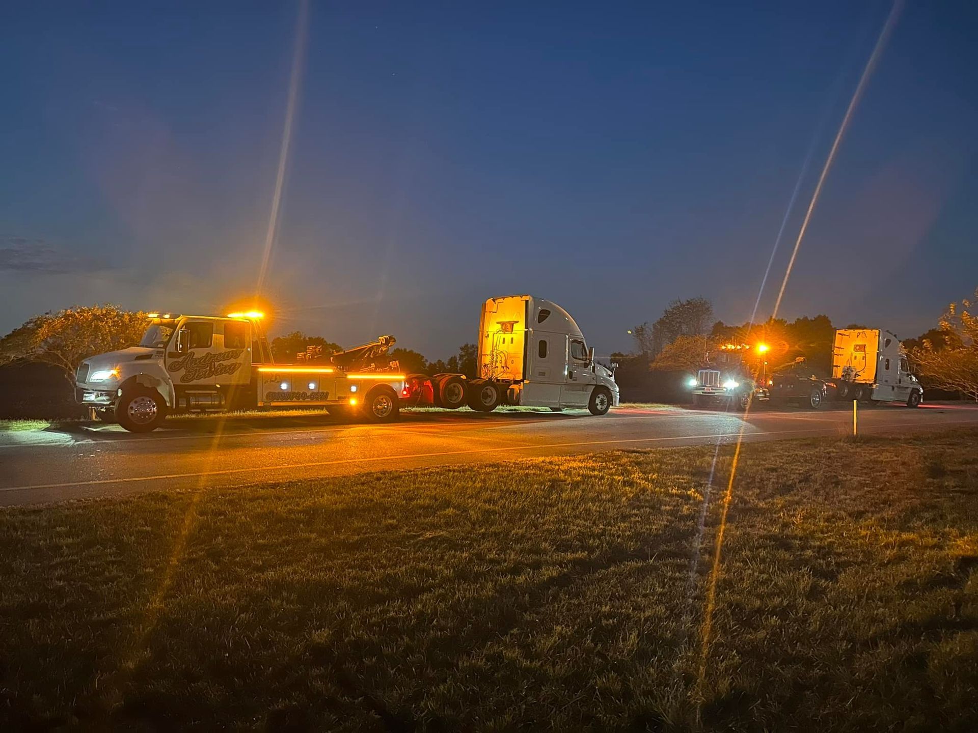 A tow truck is towing a semi truck in a parking lot at night.
