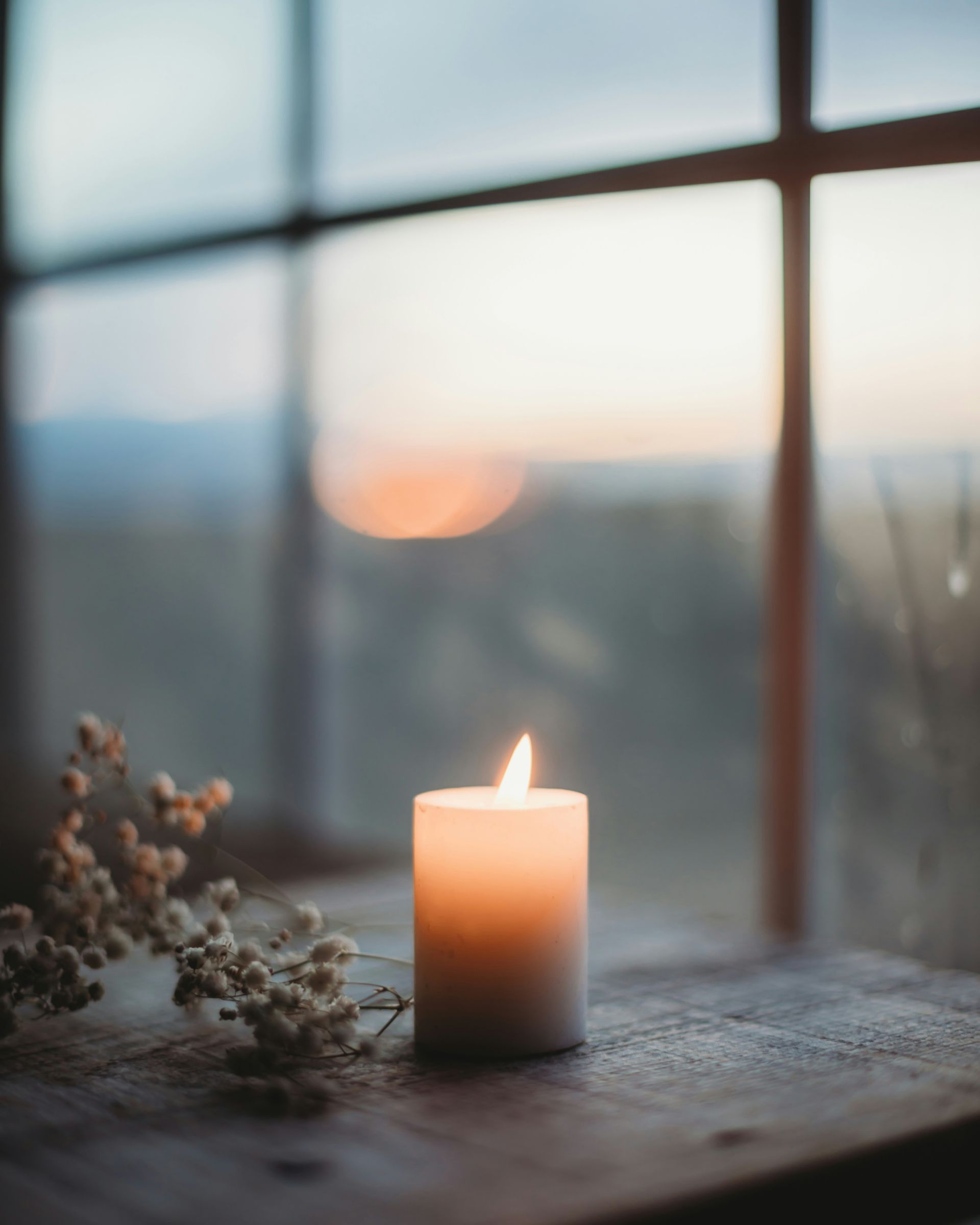 Lit candle on a windowsill at sunset with soft, blurred outdoor view