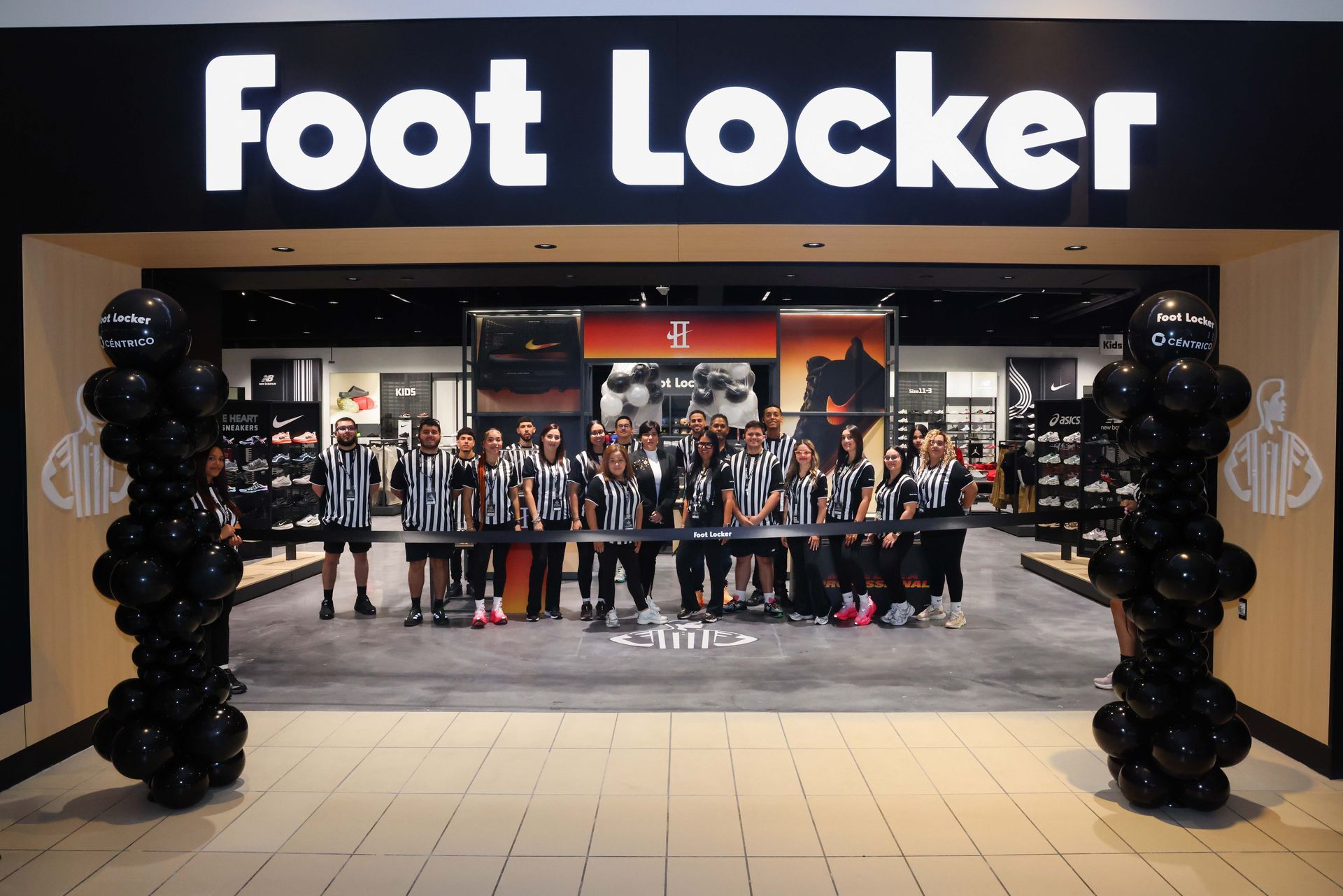 Foot Locker store opening with staff cutting ribbon; black balloons frame the entrance.