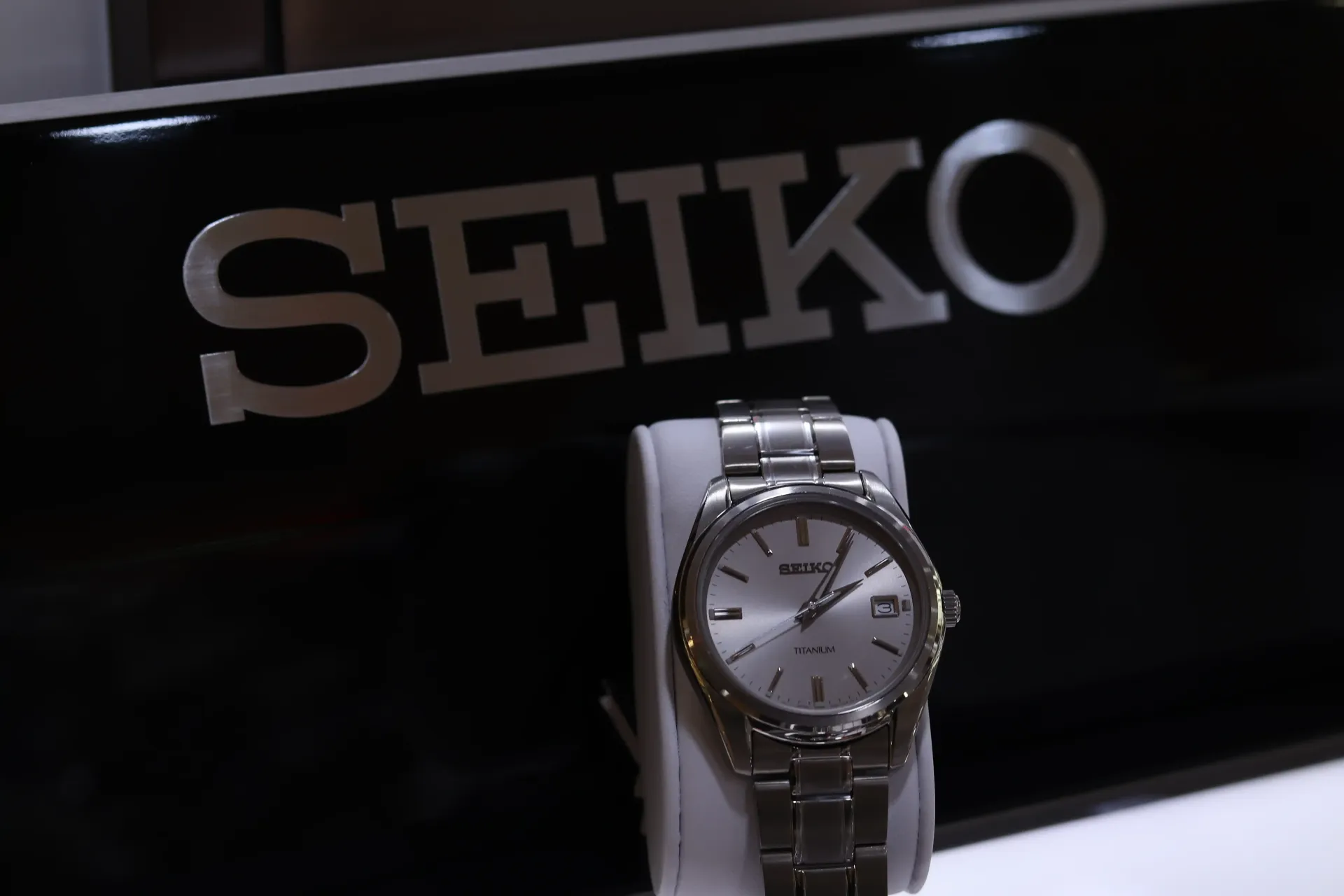 A seiko watch is displayed in front of a black sign