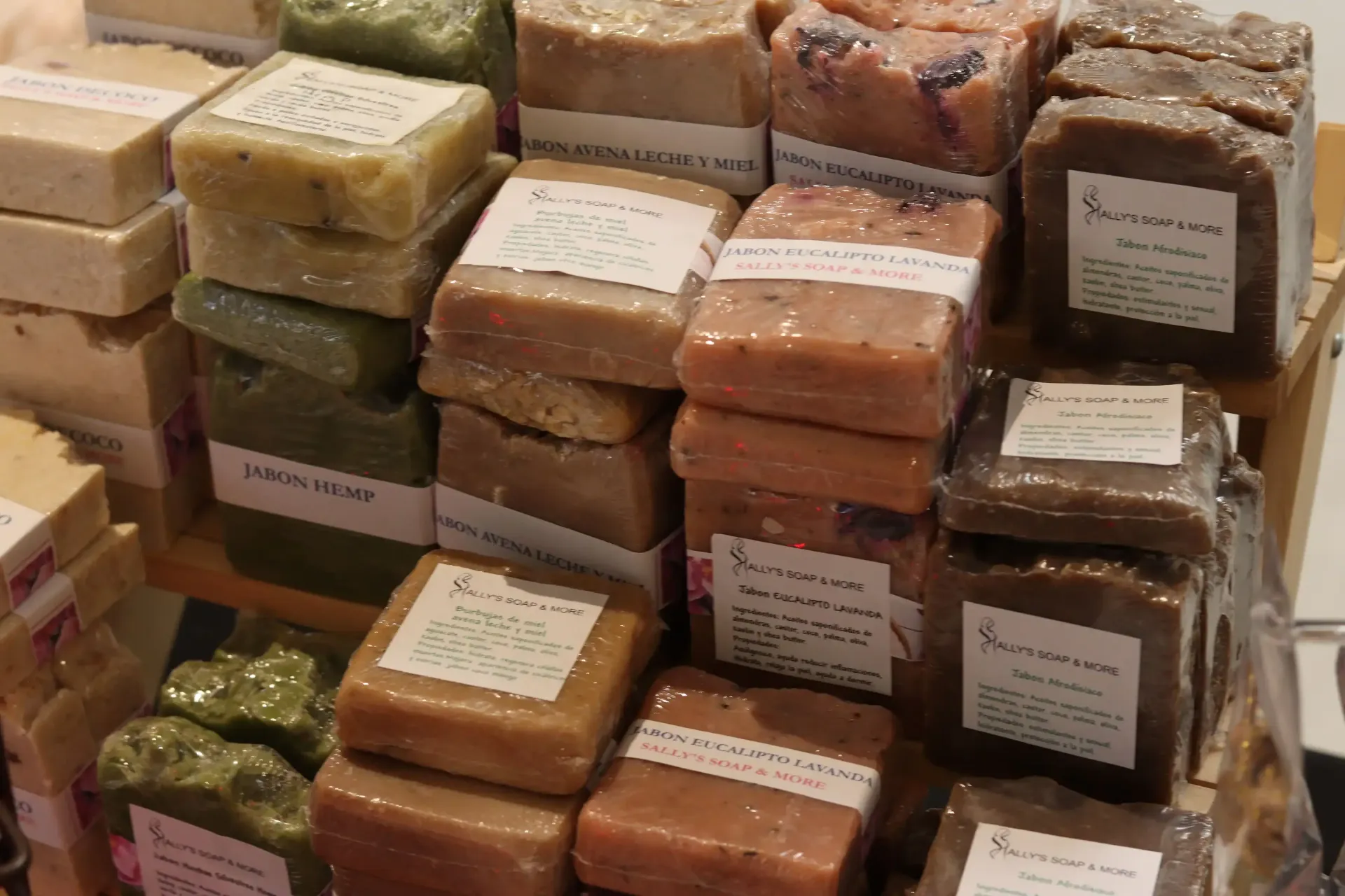 A display of various wrapped soap bars, in shades of beige, brown, and green, with white labels.