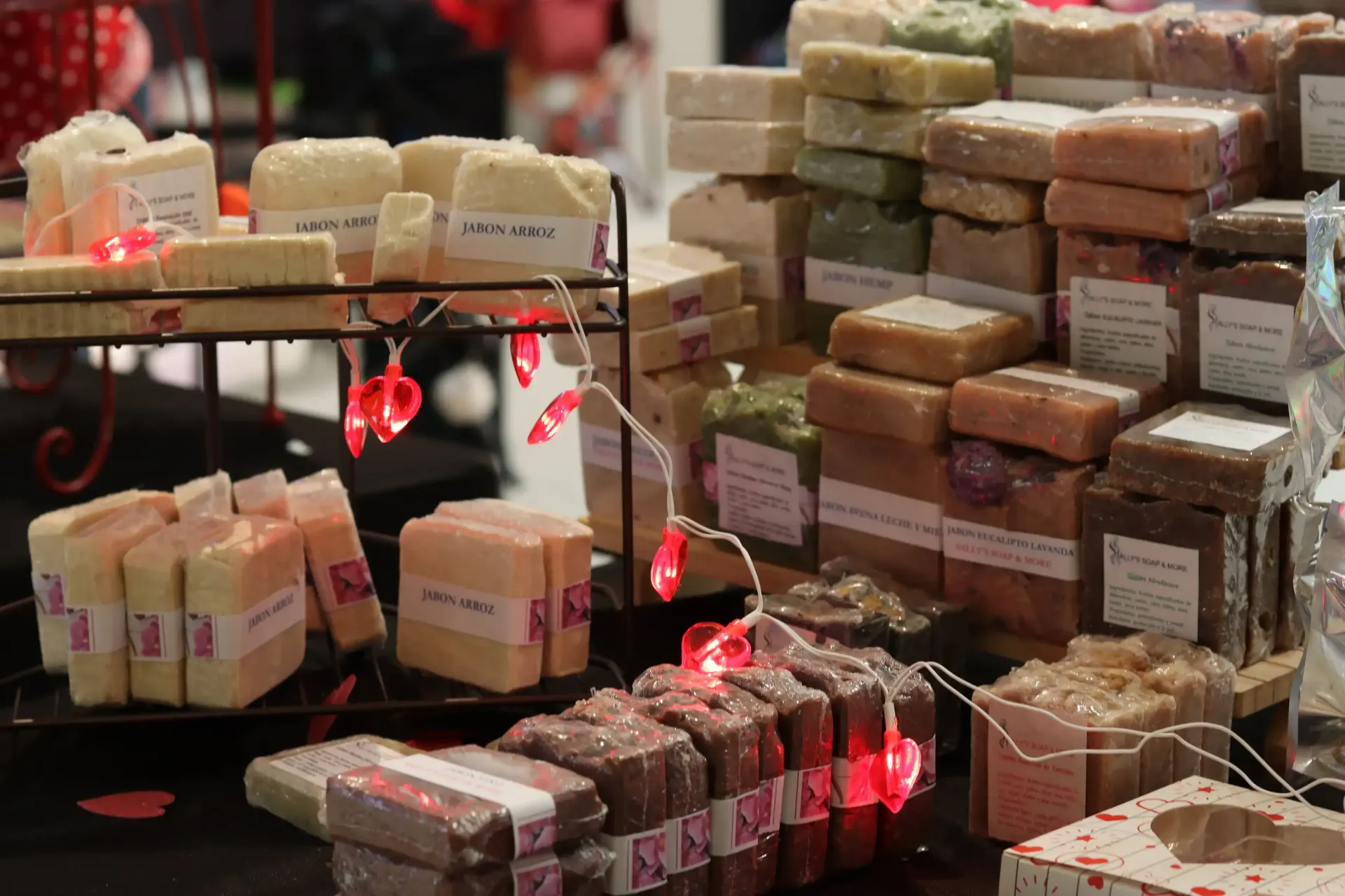 A display of handmade soaps, stacked and arranged with Valentine's Day decorations like string lights and heart accents.