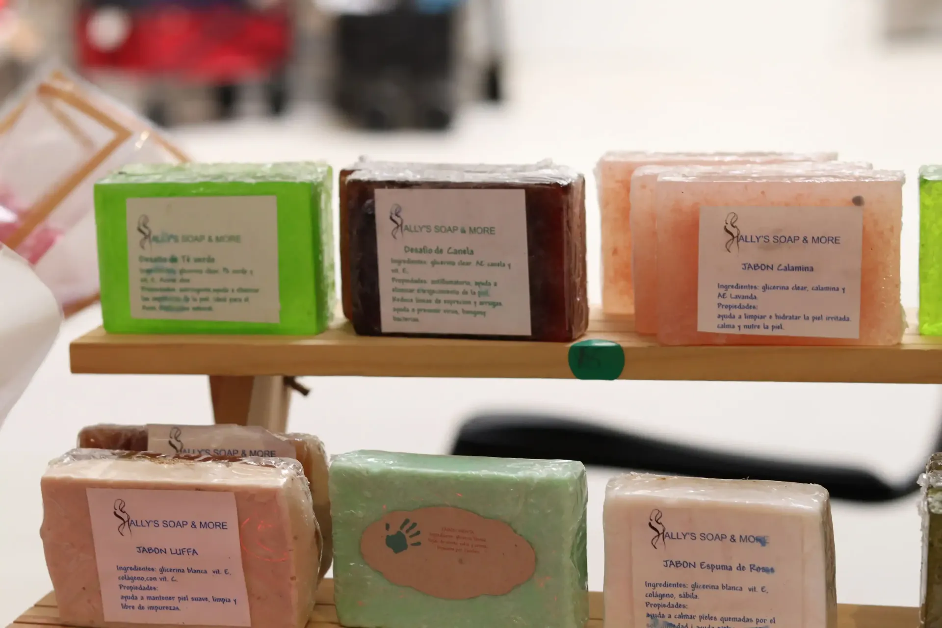 Display of colorful, square soaps on a small wooden shelf. Each soap has a label with the company logo.