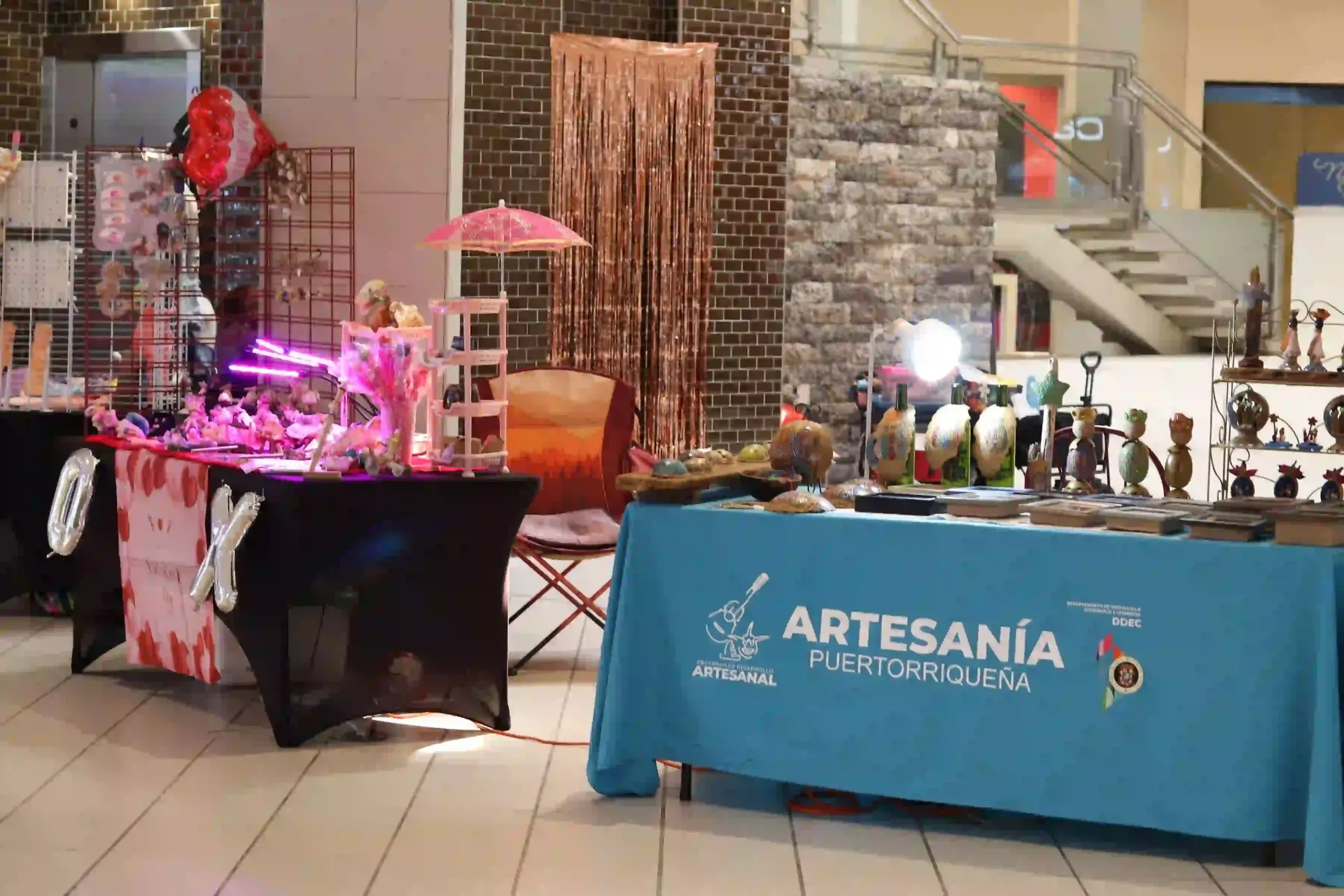 Craft fair with vendor tables displaying artisan goods indoors. One table has a blue tablecloth with