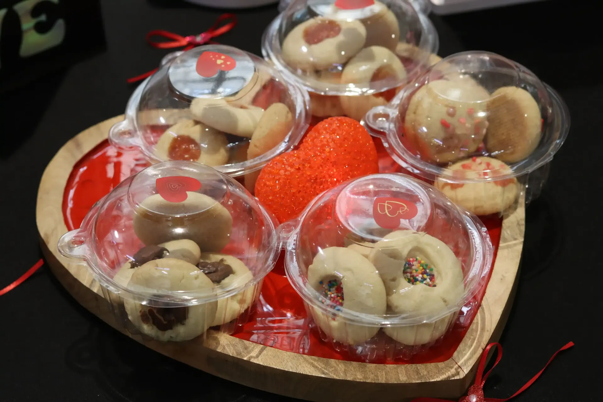 Valentine's Day treats: cookies in clear containers arranged on a heart-shaped tray, with a decorative strawberry.