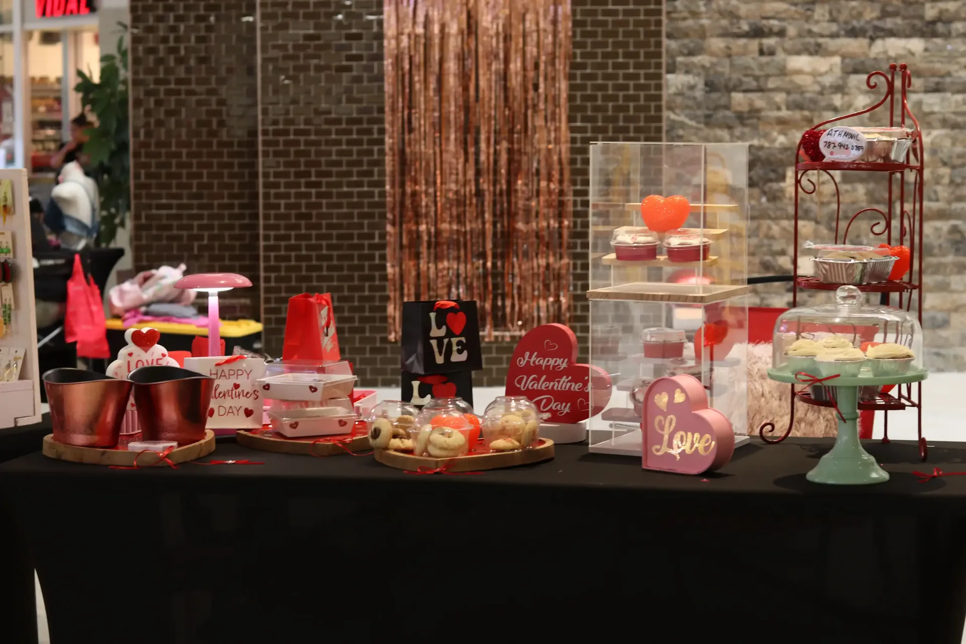 A Valentine's Day dessert display with cakes, cookies, and decorations on a black table. Red and pink colors are prominent.