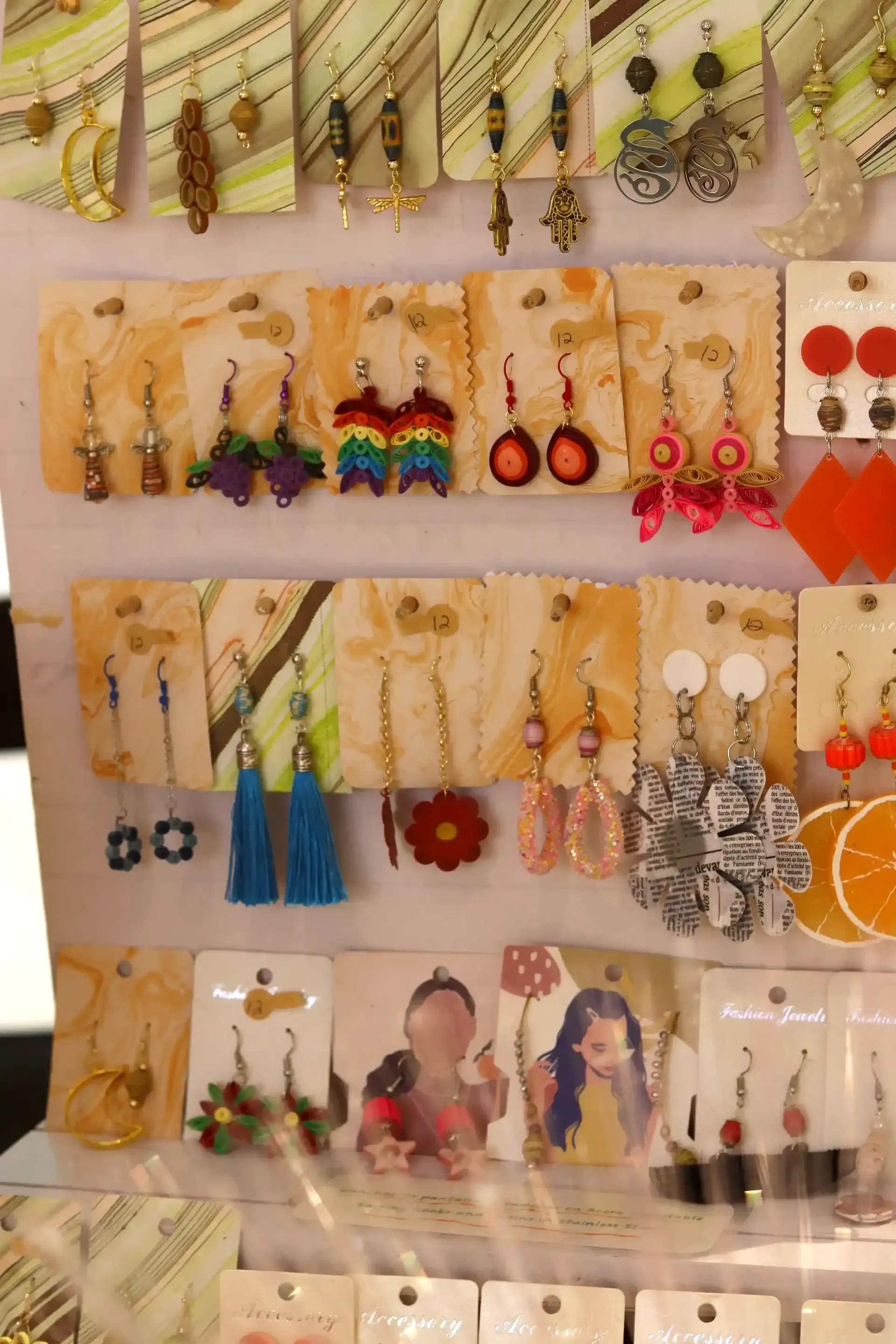 Earrings for sale displayed on a white surface. Various styles, colors, and designs are visible on individual cards.