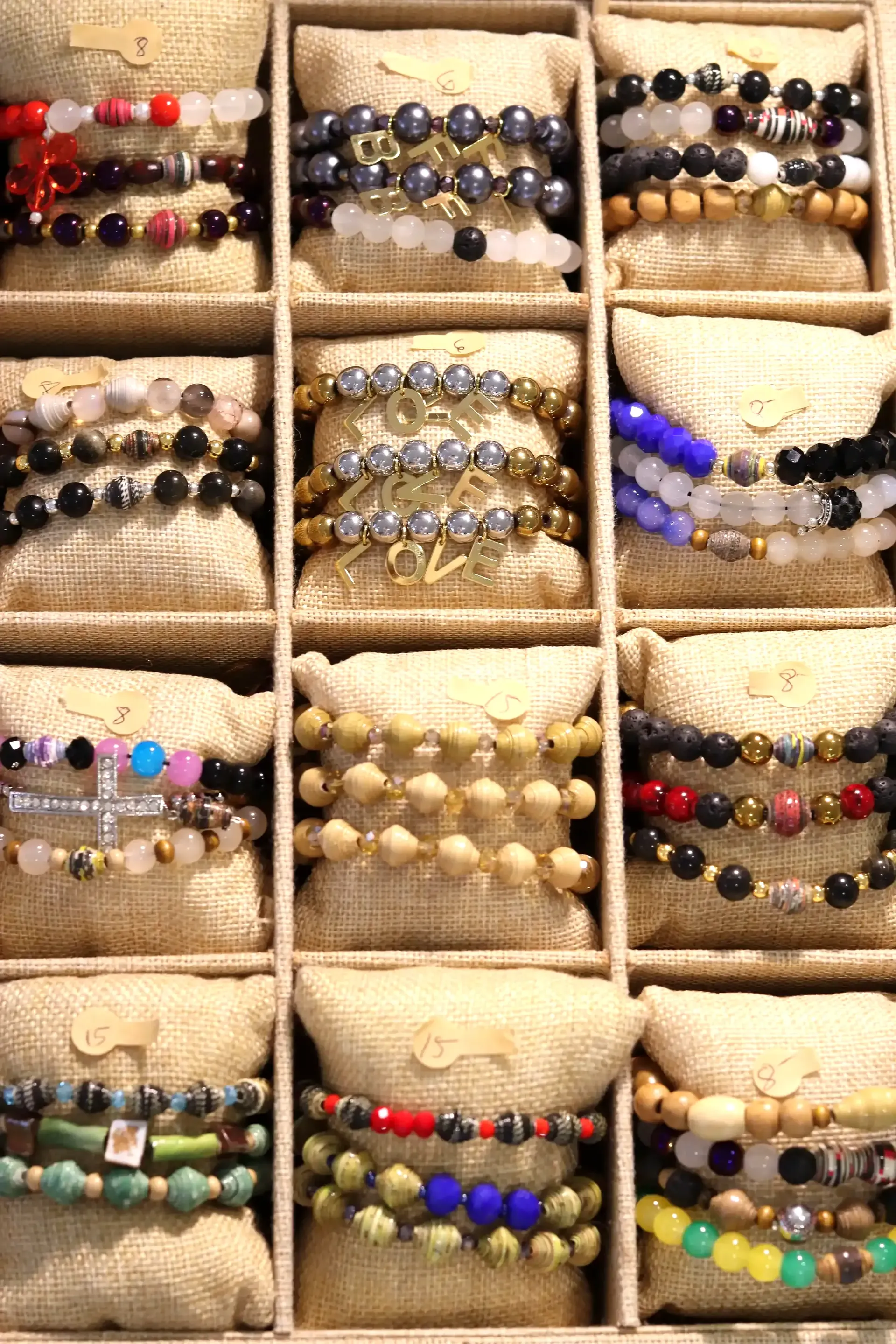 Rows of beaded bracelets displayed in a segmented box with a neutral fabric background.