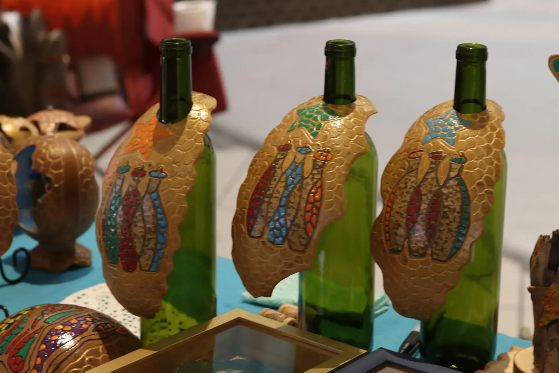 Three green wine bottles with tan, decorative tags featuring colorful vase designs on a display table.
