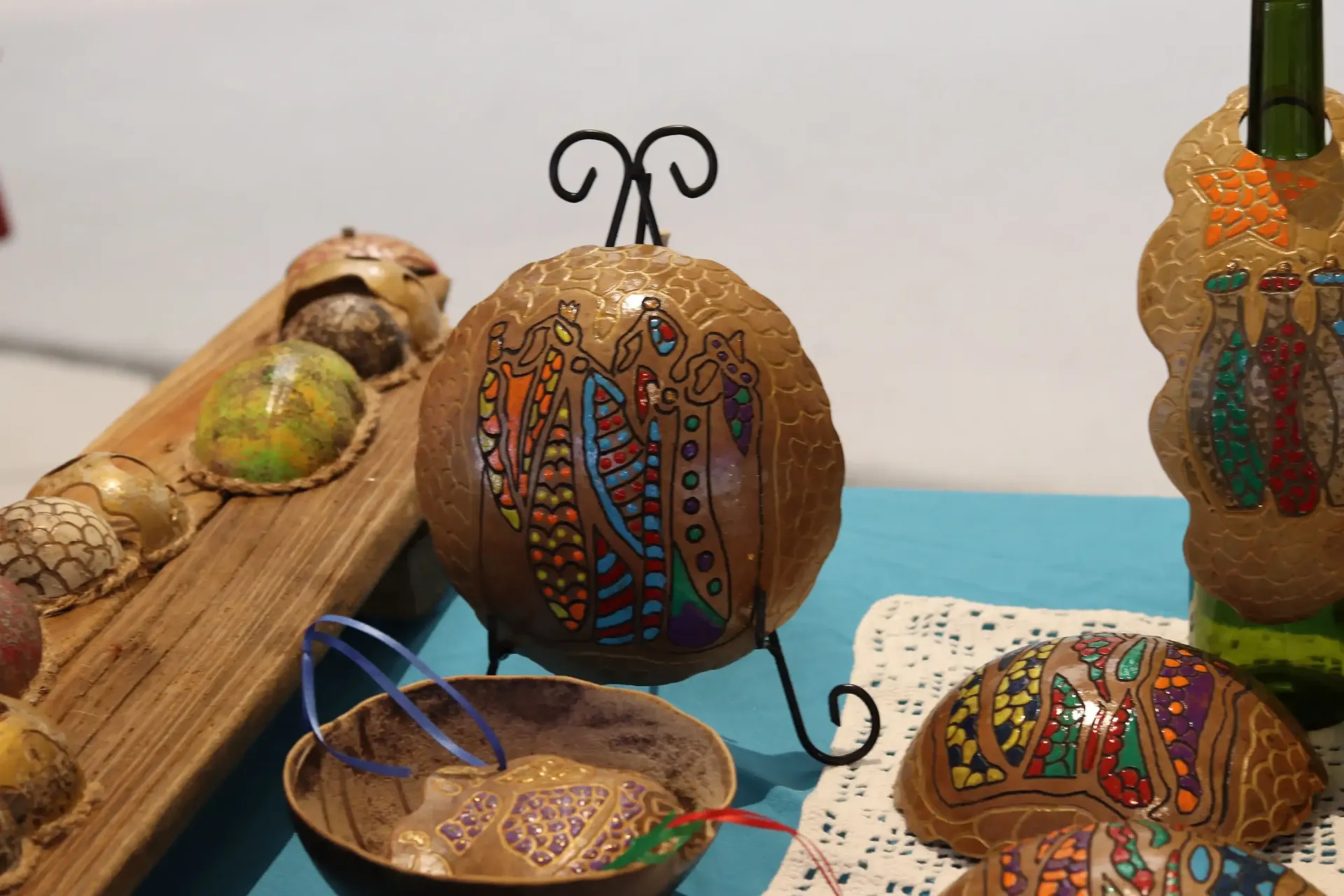 Display of decorated gourds, some on stands or in bowls, with colorful painted designs and brown wooden backgrounds.