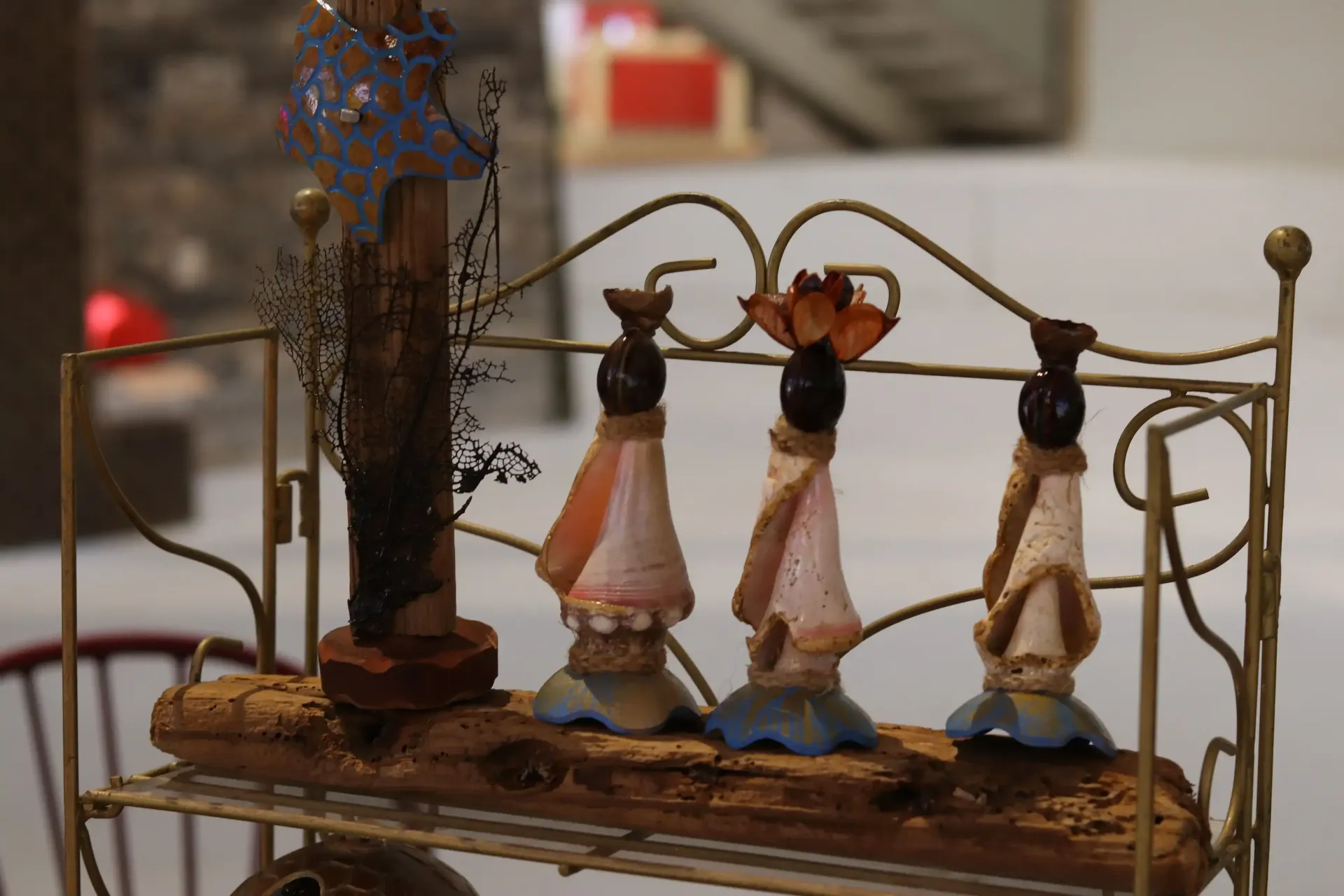 A shelf displays four decorative figures with conical dresses, each topped with a dark head and decorative elements.