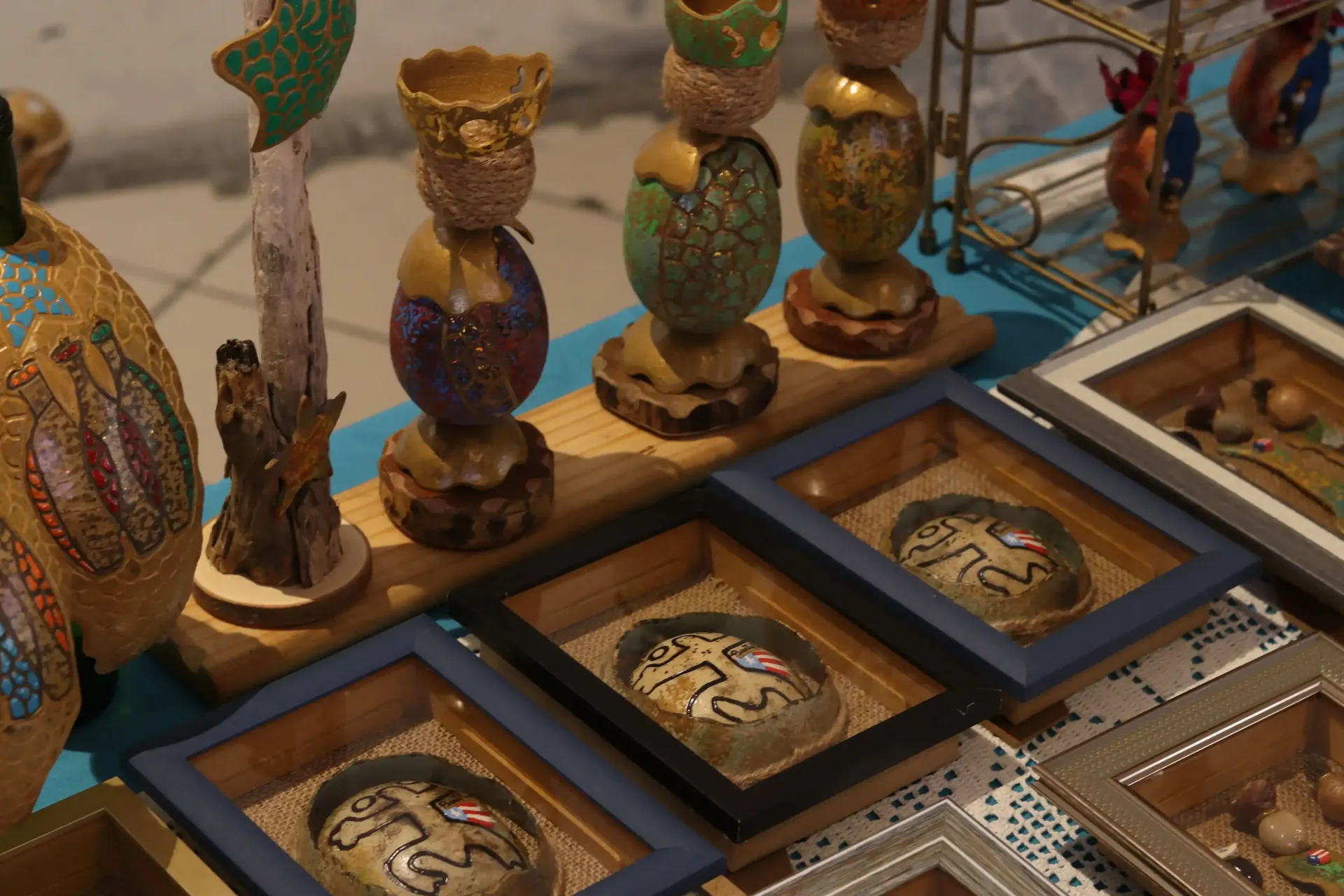 Handmade craft display with framed painted gourds and decorative egg-shaped art pieces in vibrant colors.