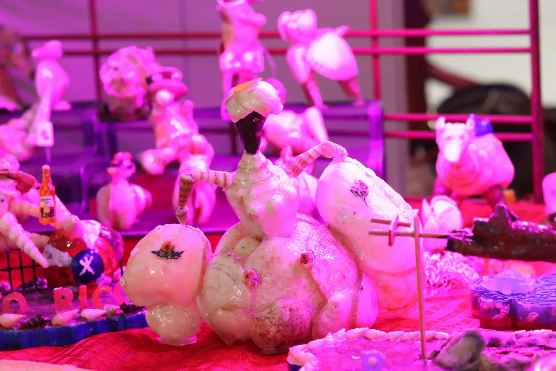 Vegetable carvings on display, lit with pink light. Figures include a dancer, animals, and miniature scenes.