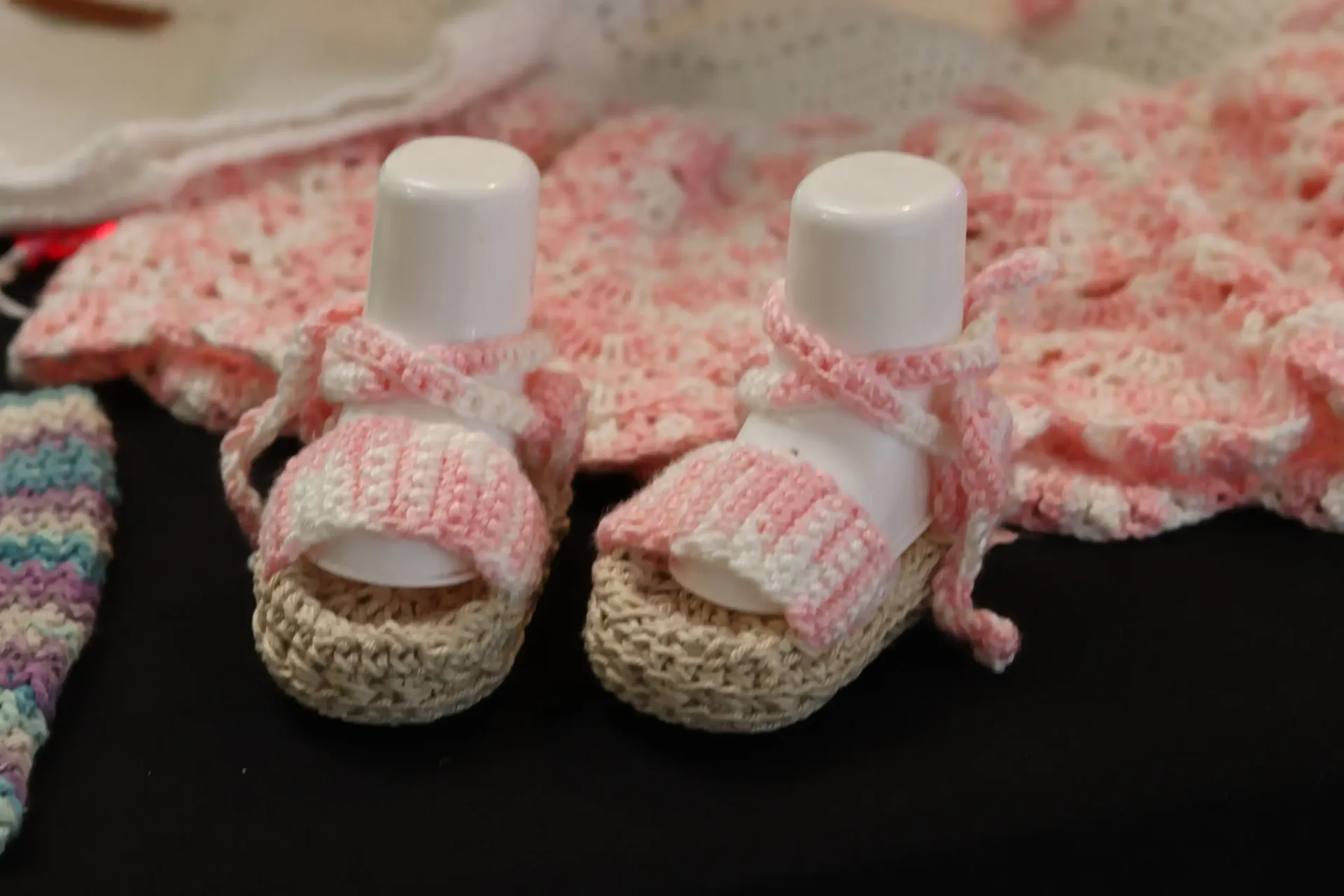 Crocheted baby sandals, light pink and white, on a light beige base, with a white tube inside.