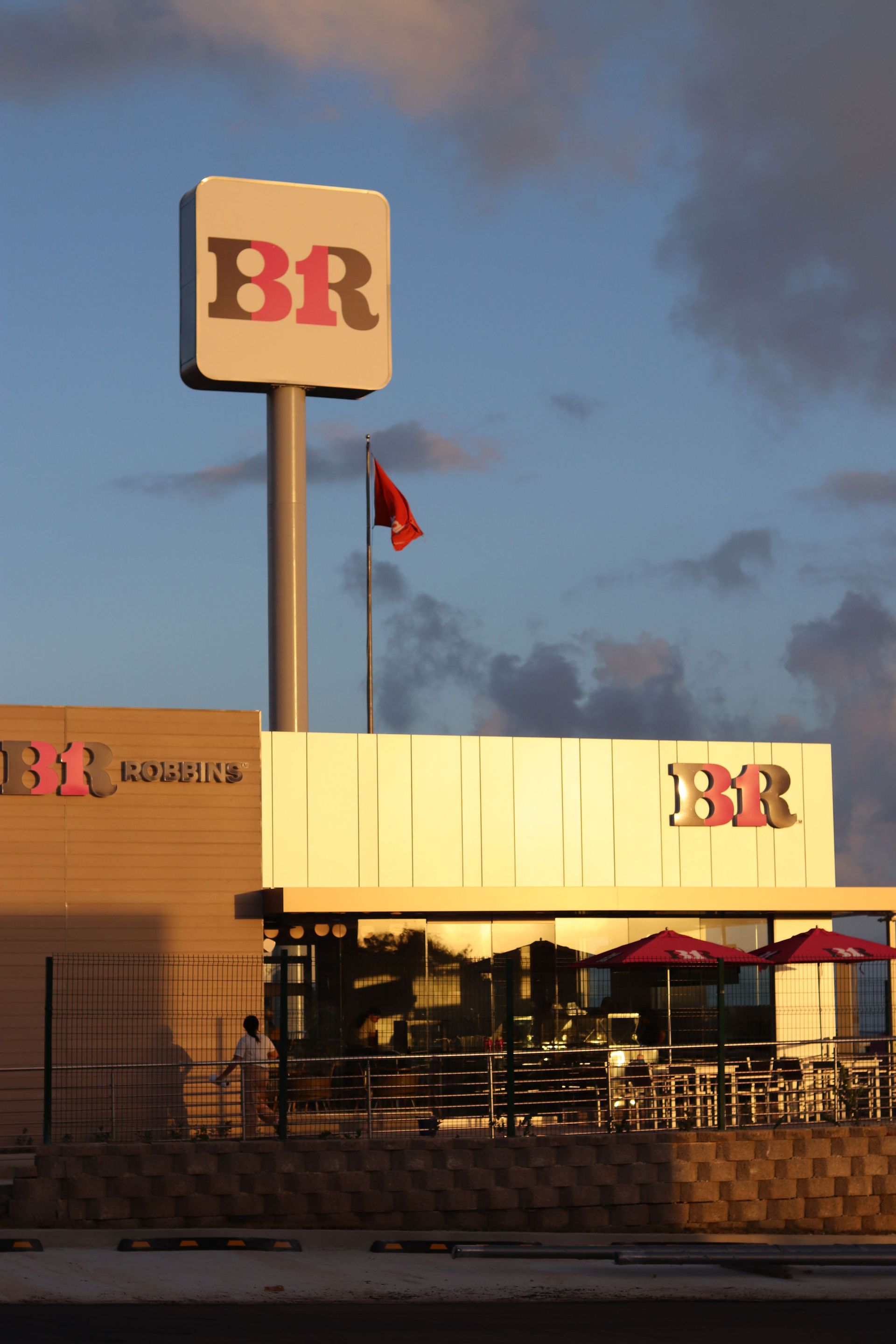 Baskin-Robbins ice cream store with a tall sign; a red flag flies in the sky.