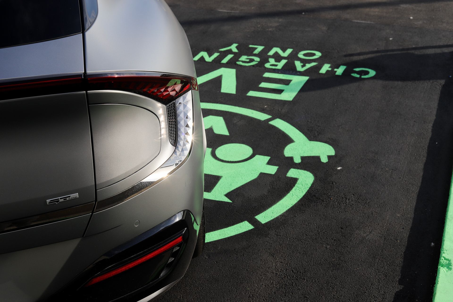 Silver electric car parked at EV charging station, green signage on asphalt.