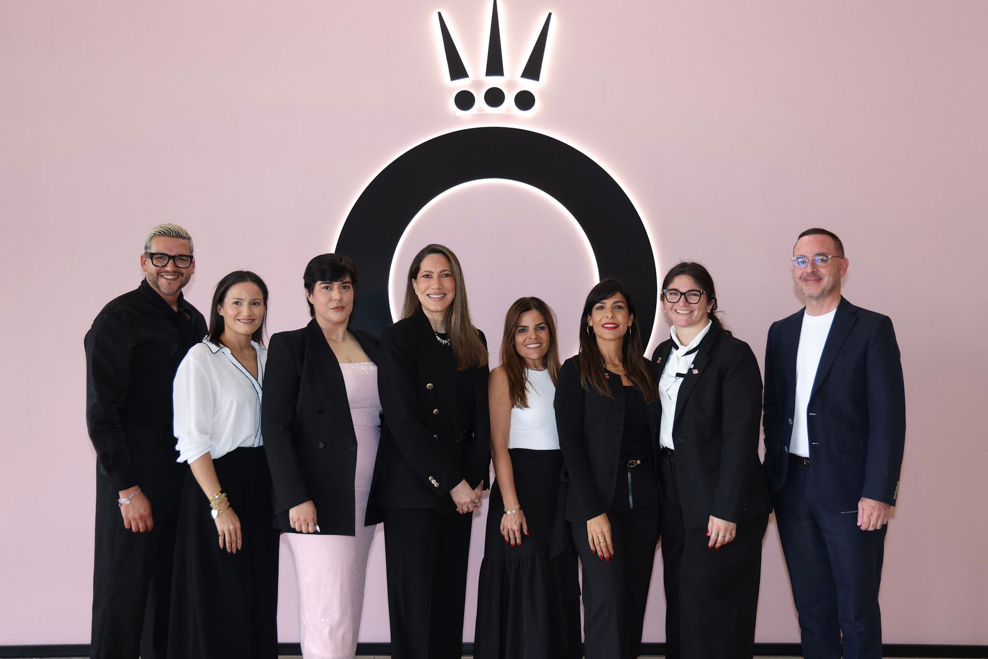 Group of people posing in front of a pink wall with a black Pandora logo.