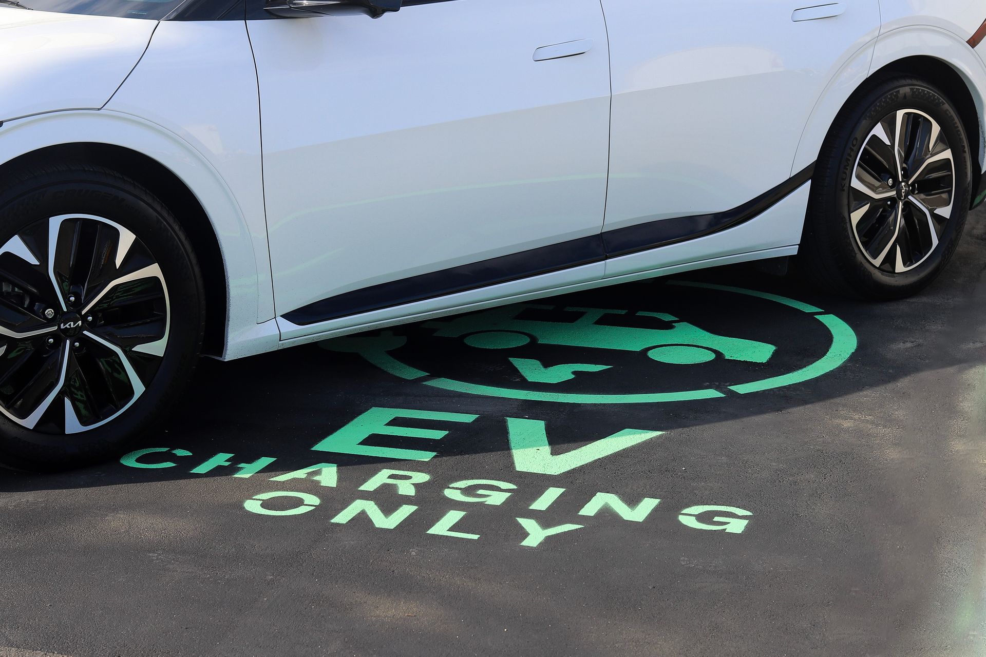 White Kia EV charging at a marked green EV charging station on asphalt.