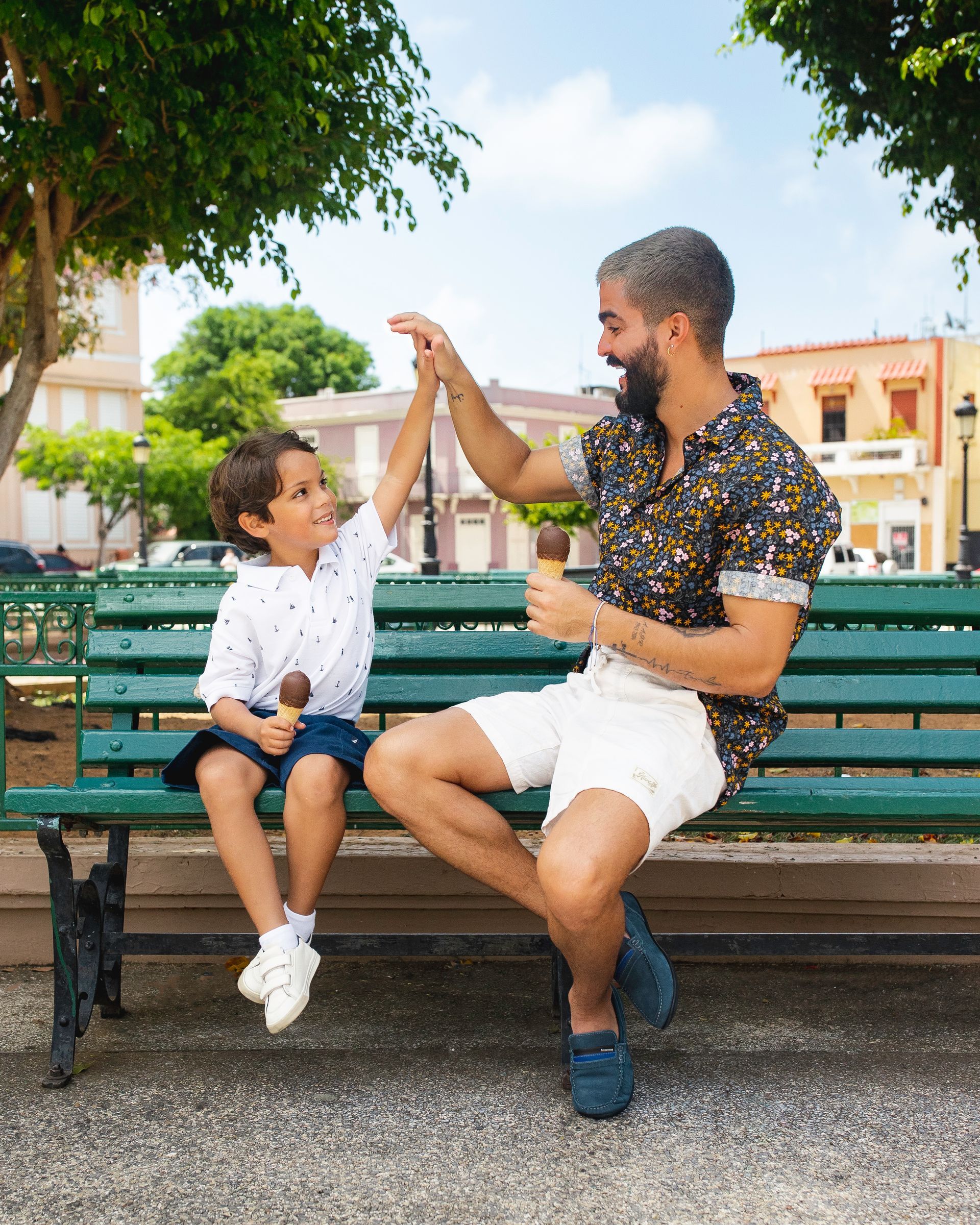 Man and child on a park bench high-five outdoors in a sunny plaza