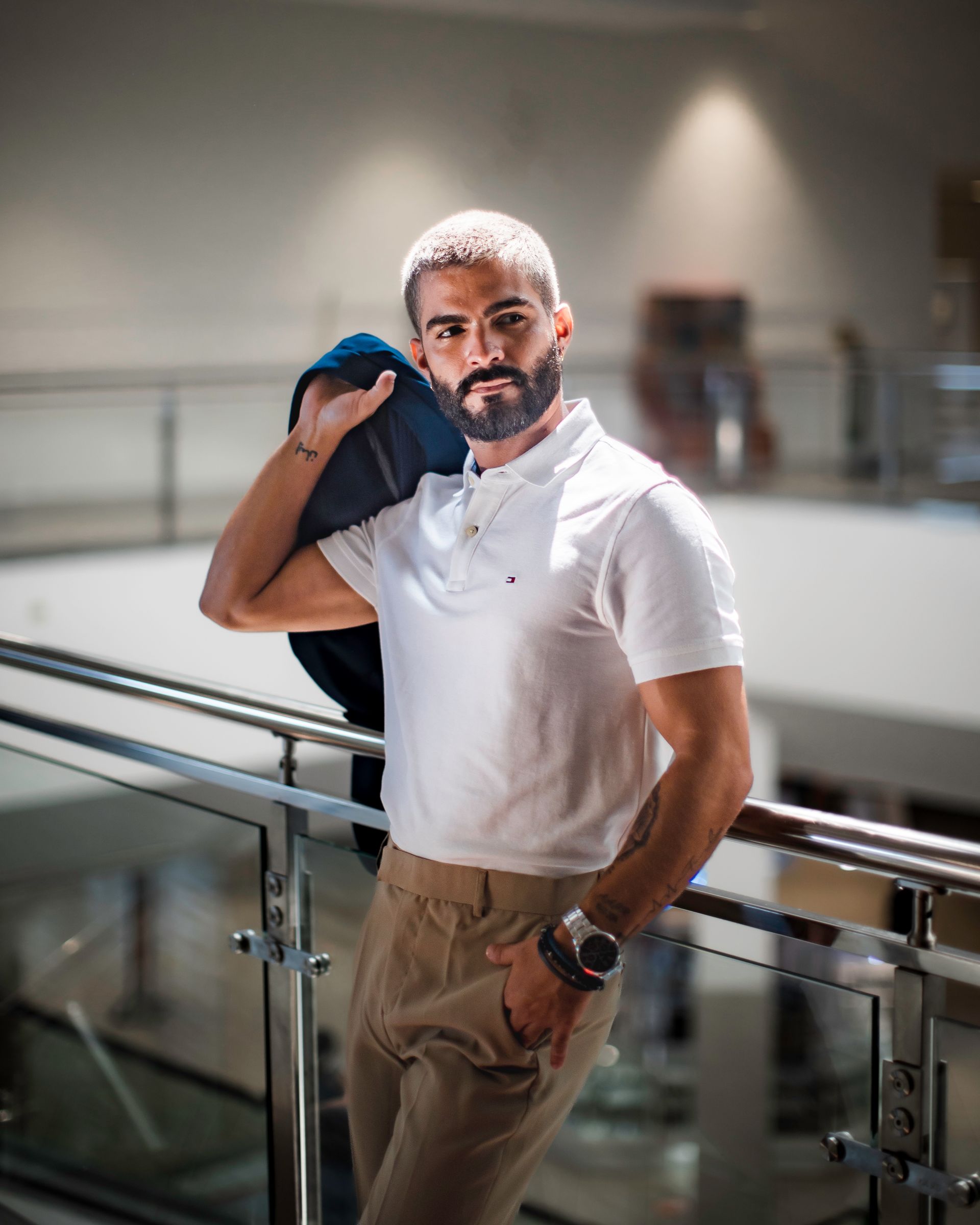 Man in white polo and khaki pants leaning on a railing in a bright indoor setting