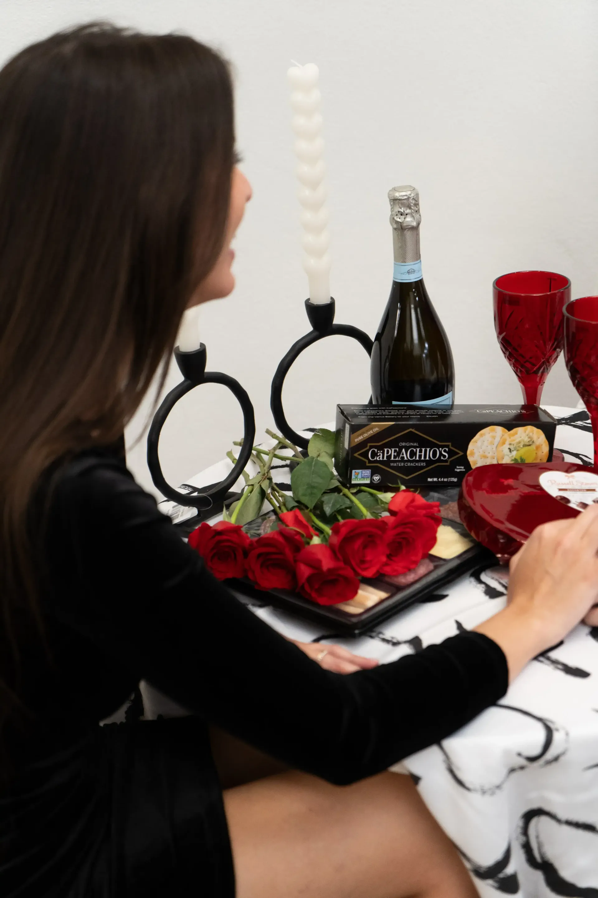 A woman is sitting at a table with a tray of roses and a bottle of champagne.