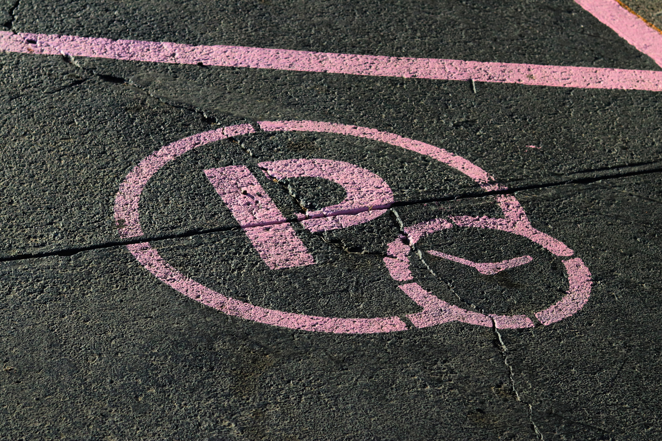 Pink parking symbol on dark asphalt with clock icon indicating timed parking.