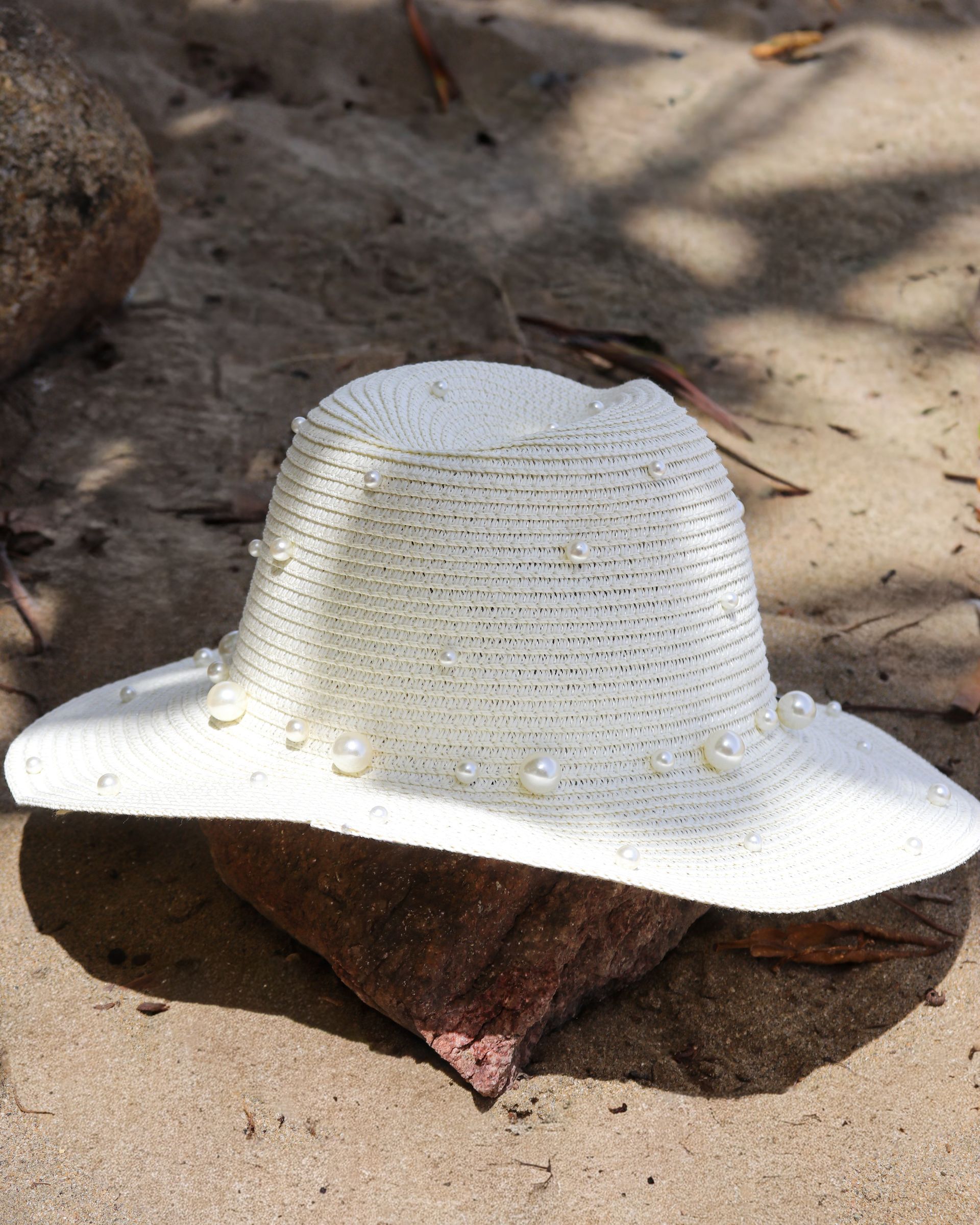 White woven sunhat resting on a rock in sandy ground
