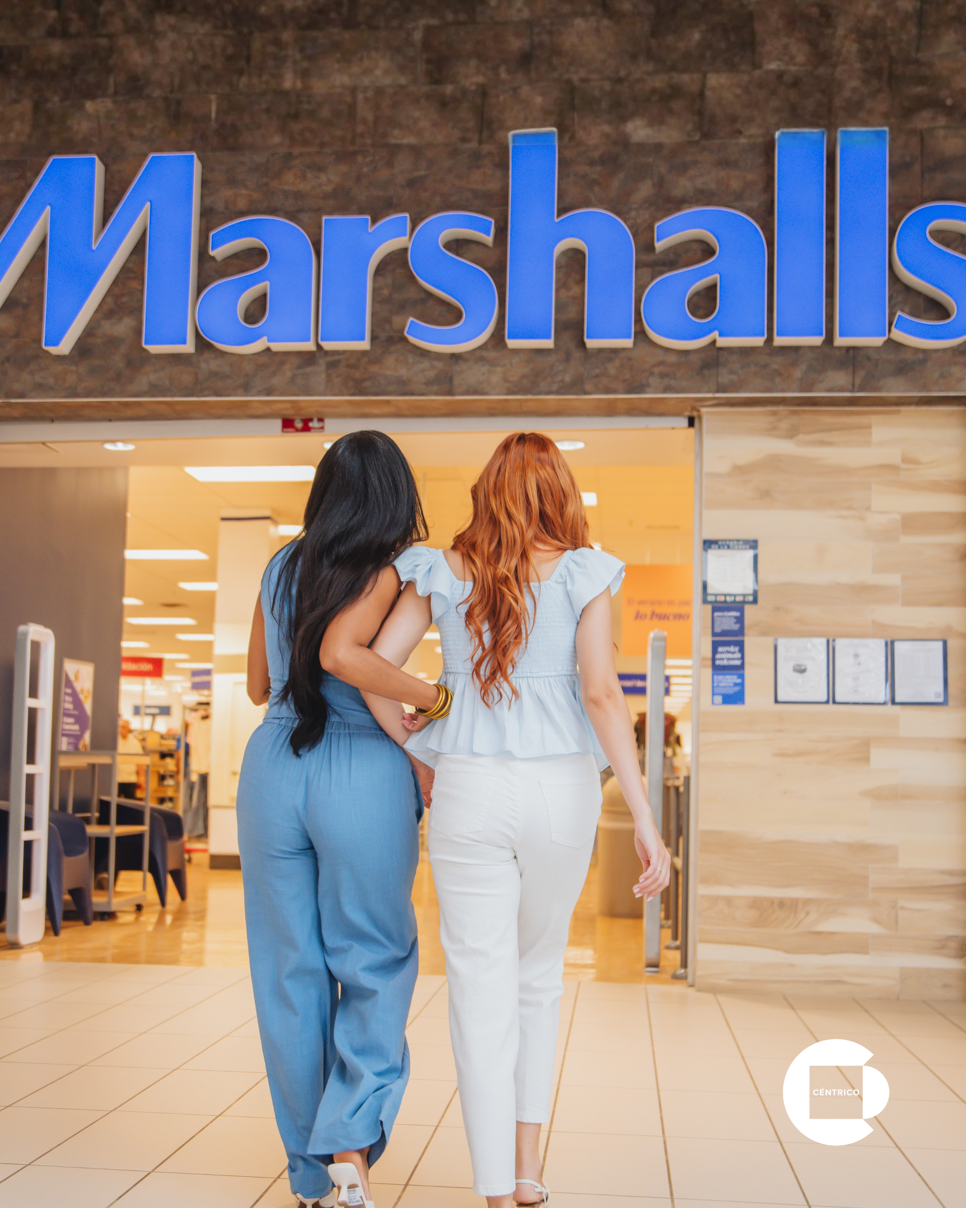 Two women walk into a Marshalls store entrance, one in blue and one in white.